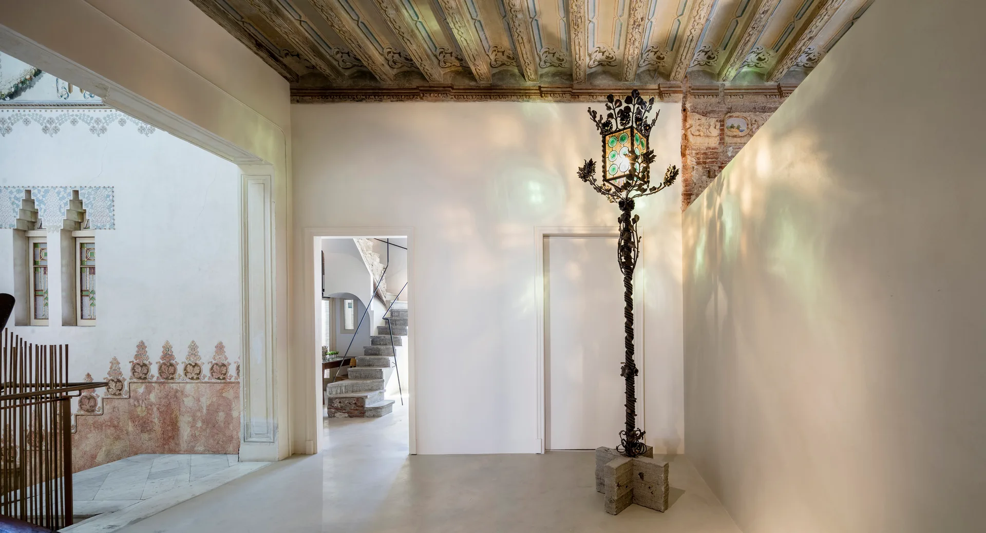 An interior corridor features white walls, a painted wood ceiling, a stone staircase, and a tall metal floor lamp casting green light reflections.
