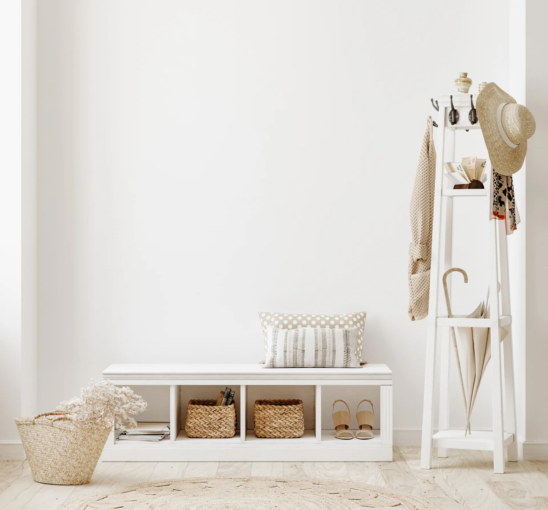An entryway features a white storage bench filled with woven baskets, a matching wooden coat rack, and a round jute rug on light wood floors.