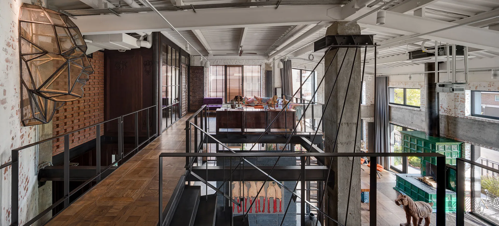 A spacious multi-level industrial loft features a black metal mezzanine staircase, a concrete column, and wood parquet flooring.