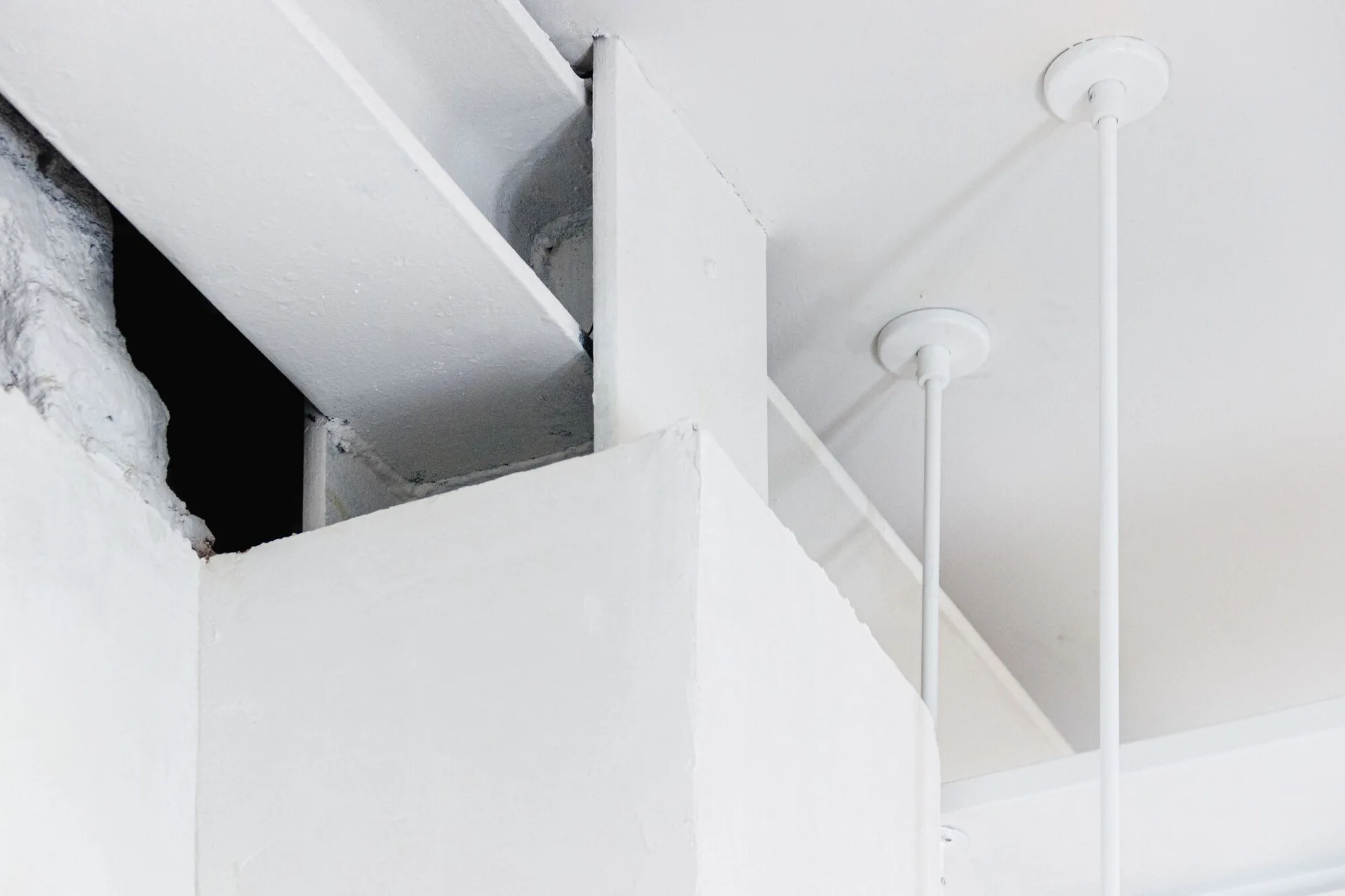 A close-up of a flat white ceiling featuring an exposed white painted steel structural beam and two thin pendant light stems.