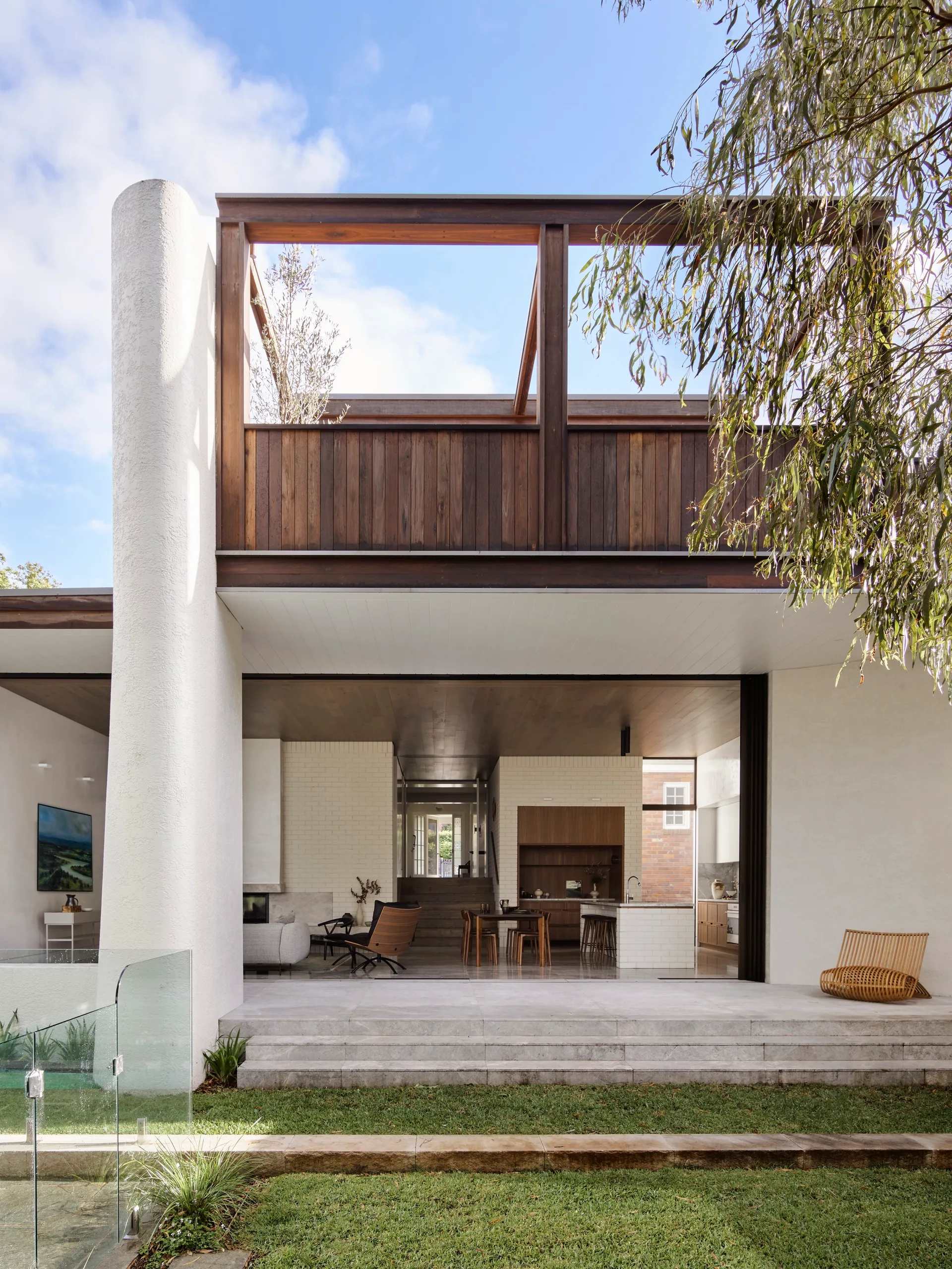 A modern home patio features wide stone steps, a large white column, and a wood-clad upper level opening into an indoor living and dining space.