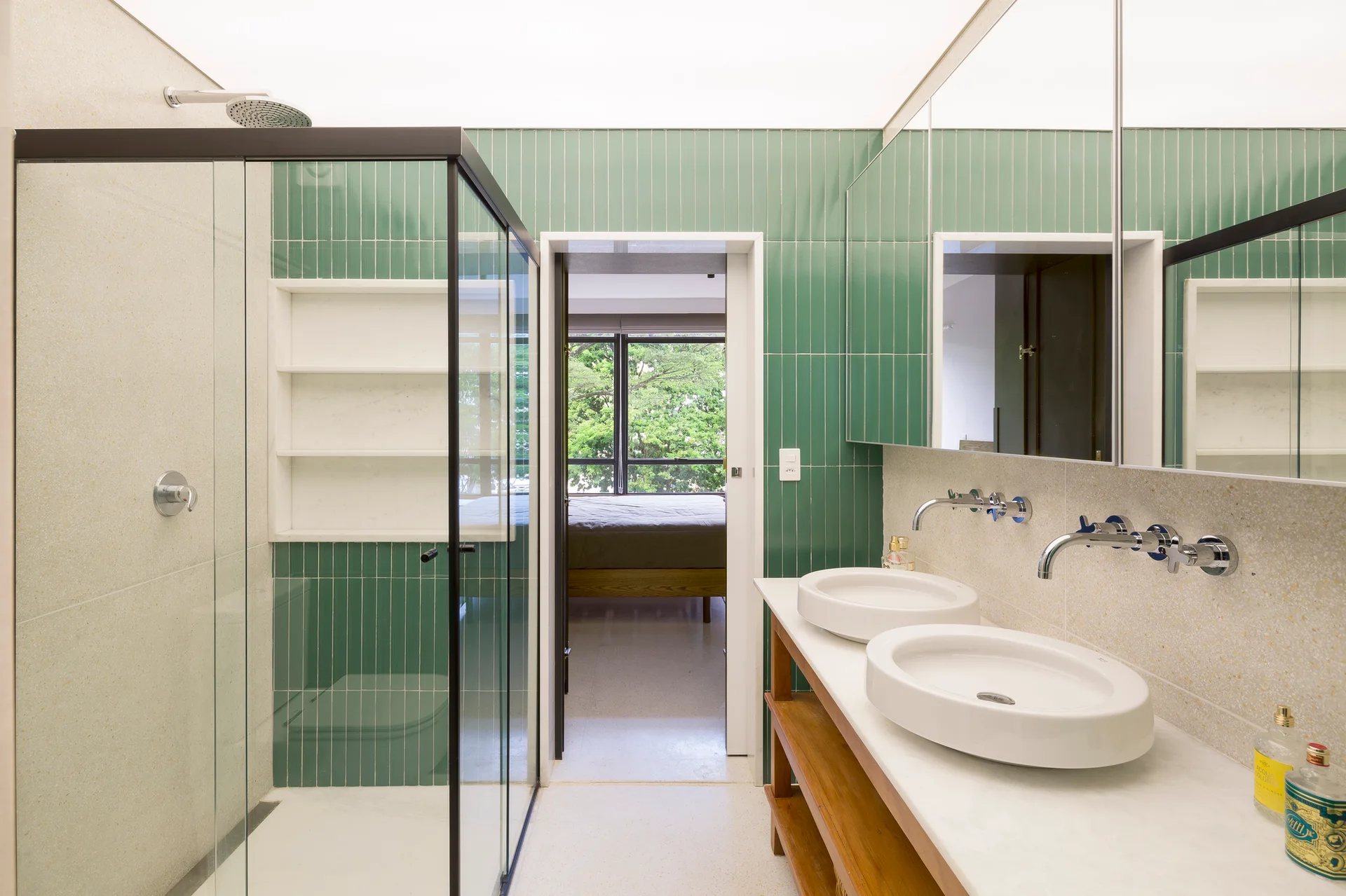 A contemporary bathroom featuring green vertical wall tiles, a glass shower with a black frame, and a double vanity with round vessel sinks.