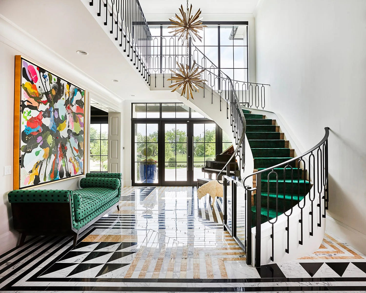 A grand entryway features a curved staircase with a green runner, a bold geometric marble floor, and a large colorful abstract painting.