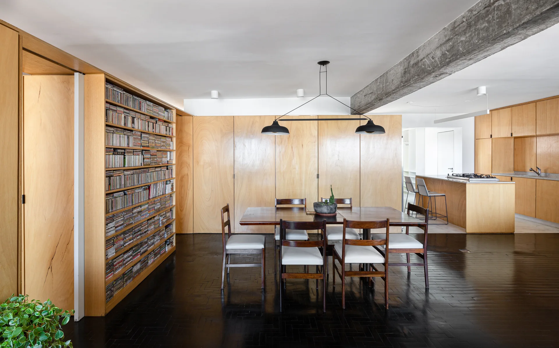 A modern dining room features a dark wood table and chairs beneath a black pendant light, surrounded by light wood wall paneling and a dark herringbone floor.