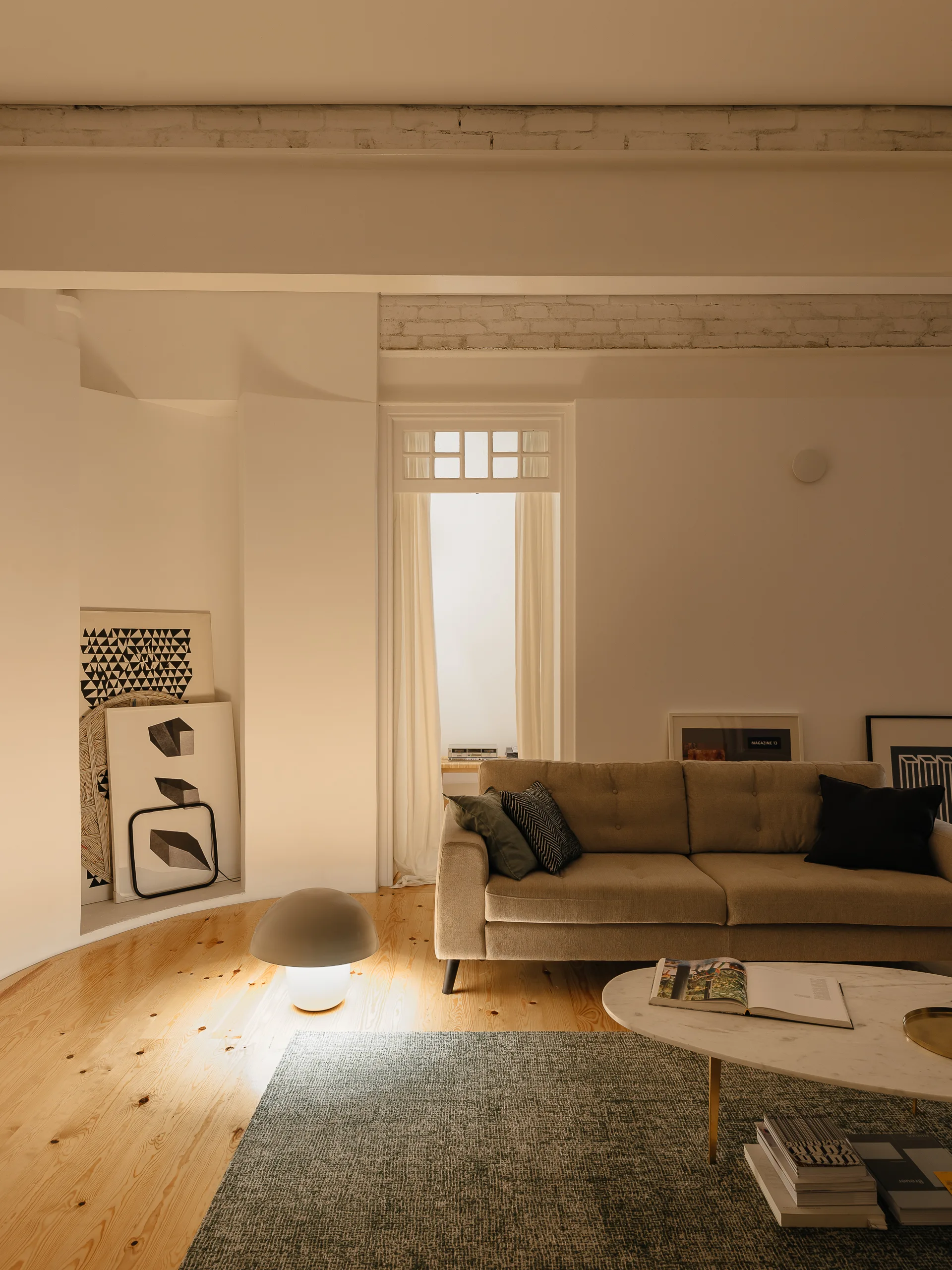 A minimalist living room features a beige sofa, a green textured rug, and a glowing mushroom floor lamp on light wood floors.