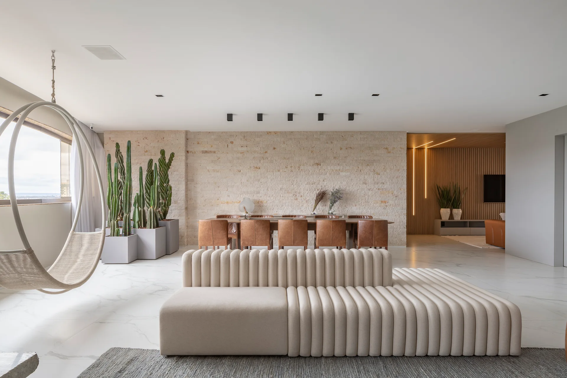 A contemporary open-plan living and dining area with a cream channeled sofa, a circular hanging chair, and a stone-clad feature wall.