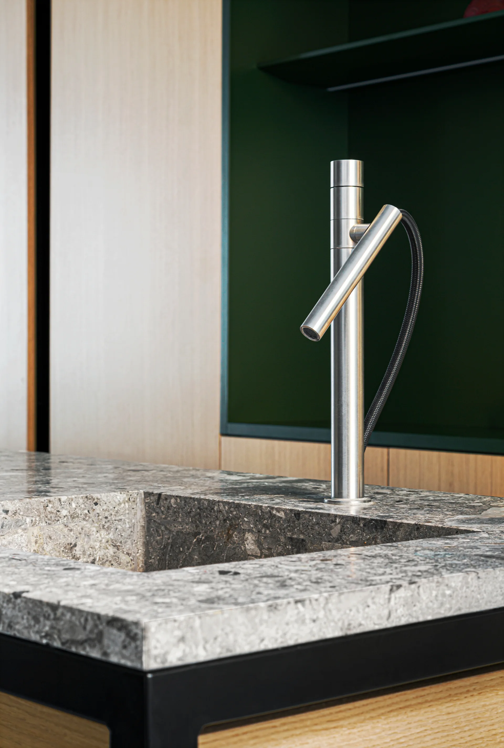 A close-up of a modern kitchen island featuring an integrated grey stone sink and a brushed metal faucet with a dark green cabinet background.