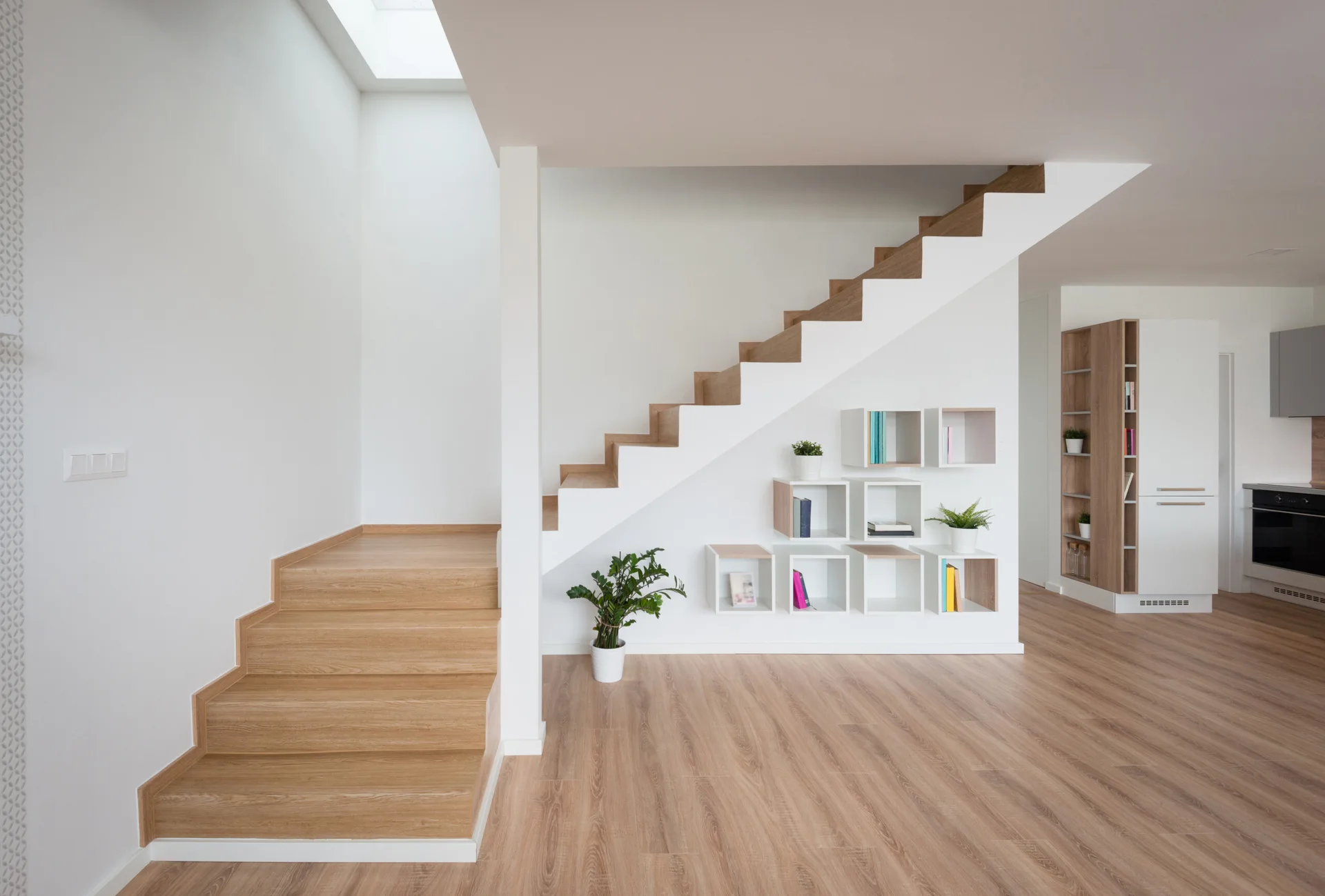 A light wood staircase ascends next to modular square shelves mounted on a white wall, set over light wood-plank flooring.