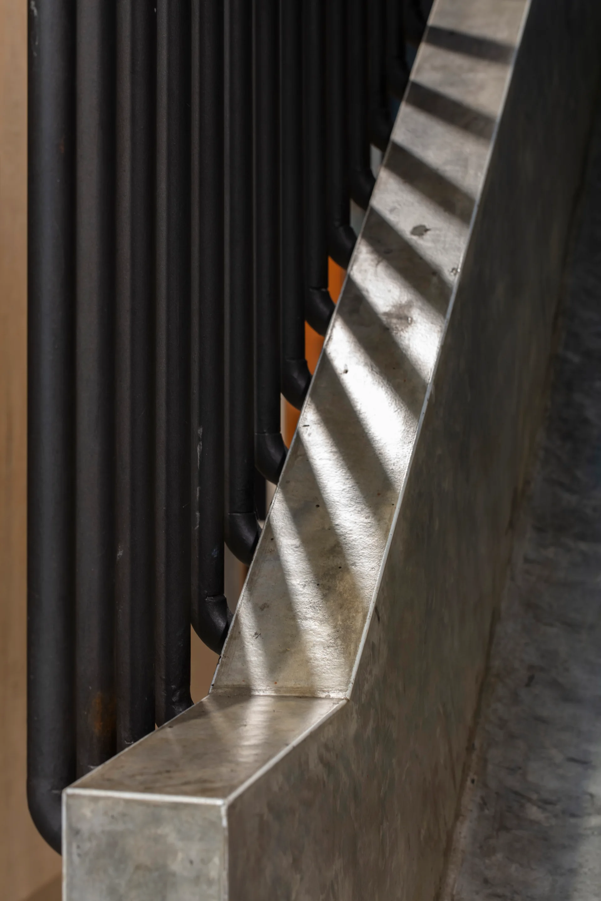 A close-up view of a modern staircase railing featuring vertical black metal balusters alongside a grey concrete handrail with cast shadows.
