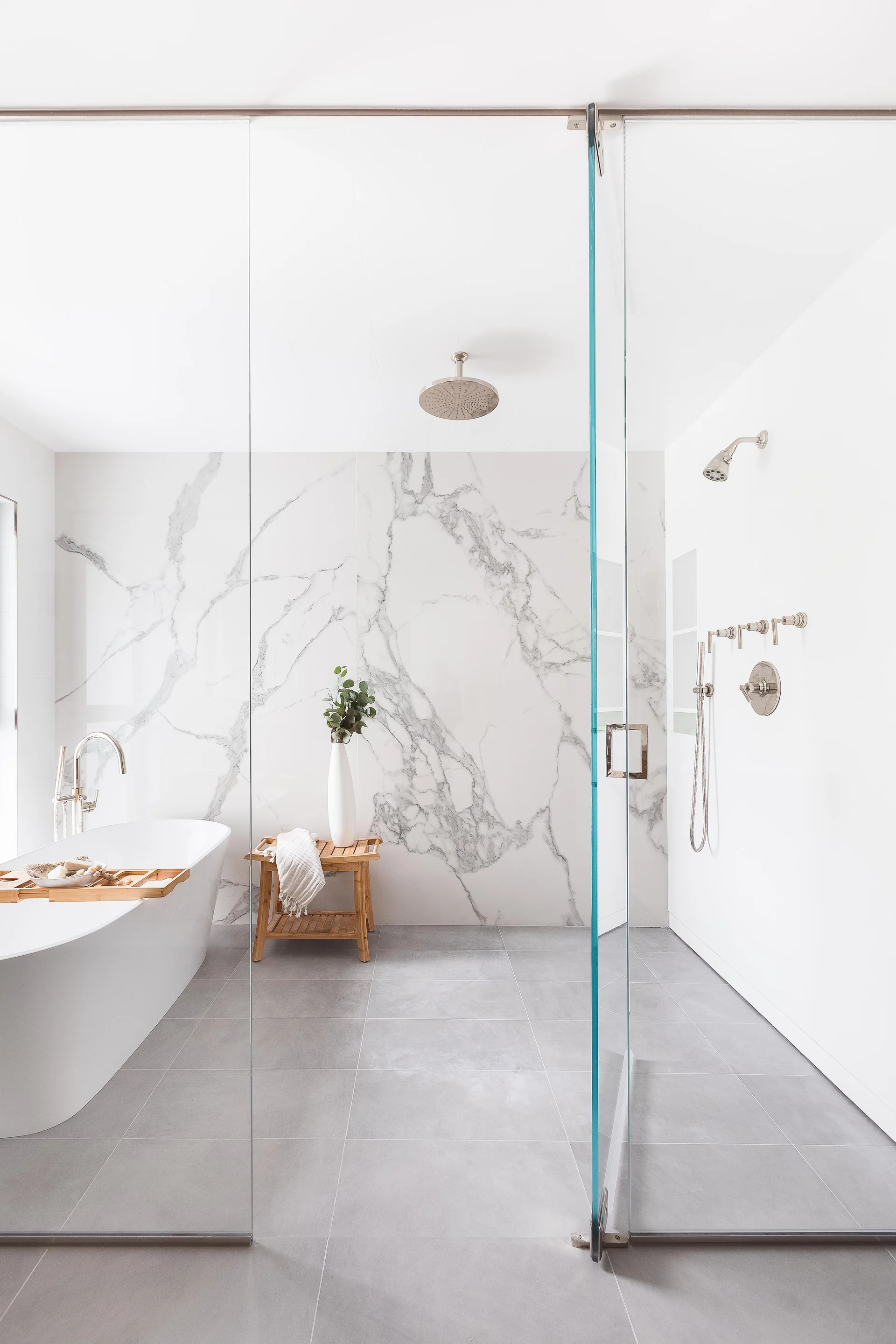 A modern white bathroom features a freestanding bathtub, a glass shower partition, and a large grey-veined marble slab accent wall.
