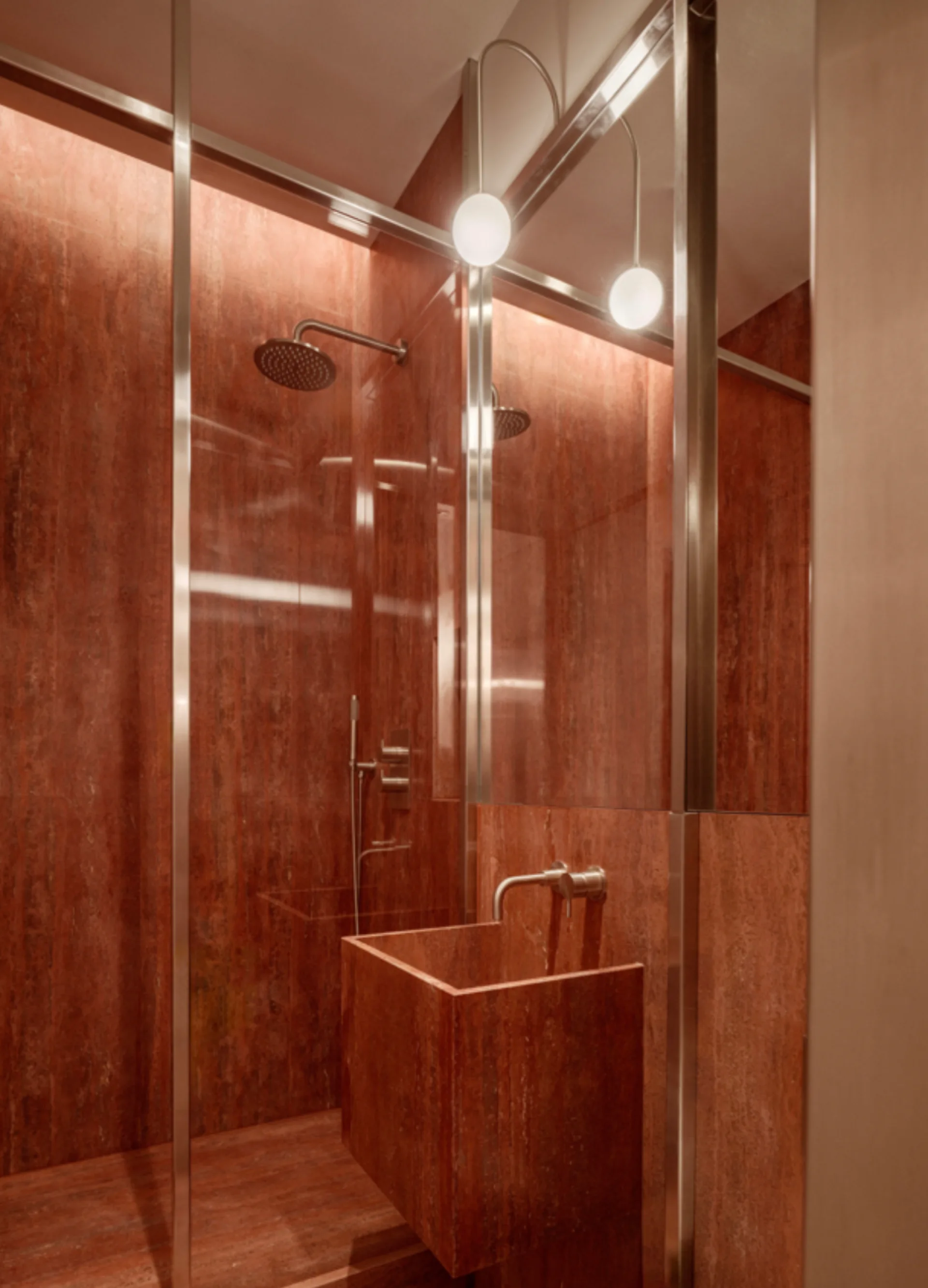 A modern bathroom featuring walls and a floating block sink clad in red veined stone, next to a metal-framed glass shower enclosure.