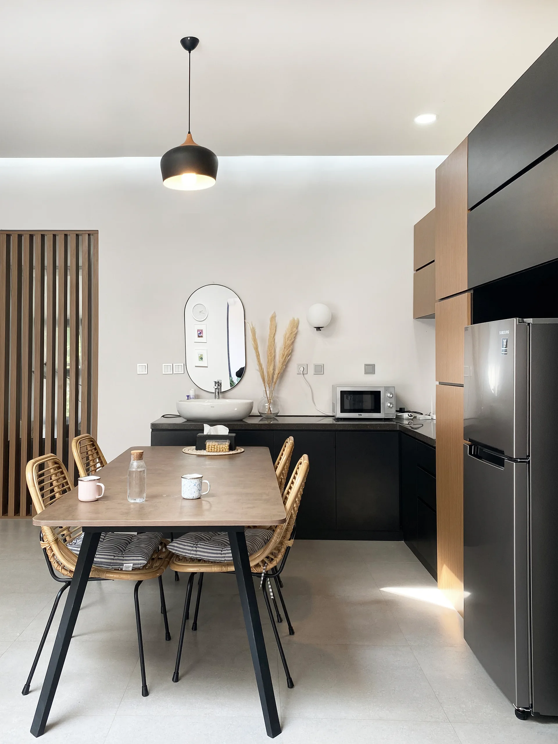 A modern kitchen and dining space featuring matte black and wood cabinetry, a dining table with rattan chairs, and a countertop vessel sink with a mirror.