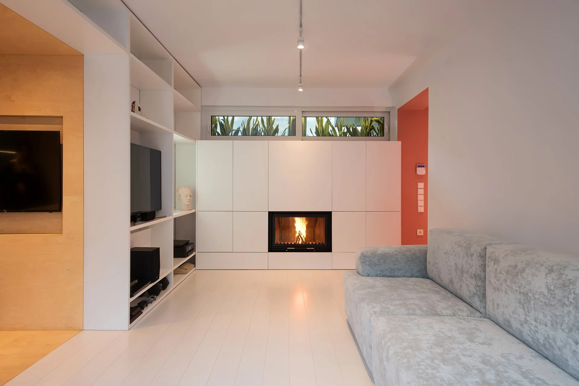 A modern living room features a white built-in storage unit with an integrated fireplace, a light grey sofa, and white plank flooring.