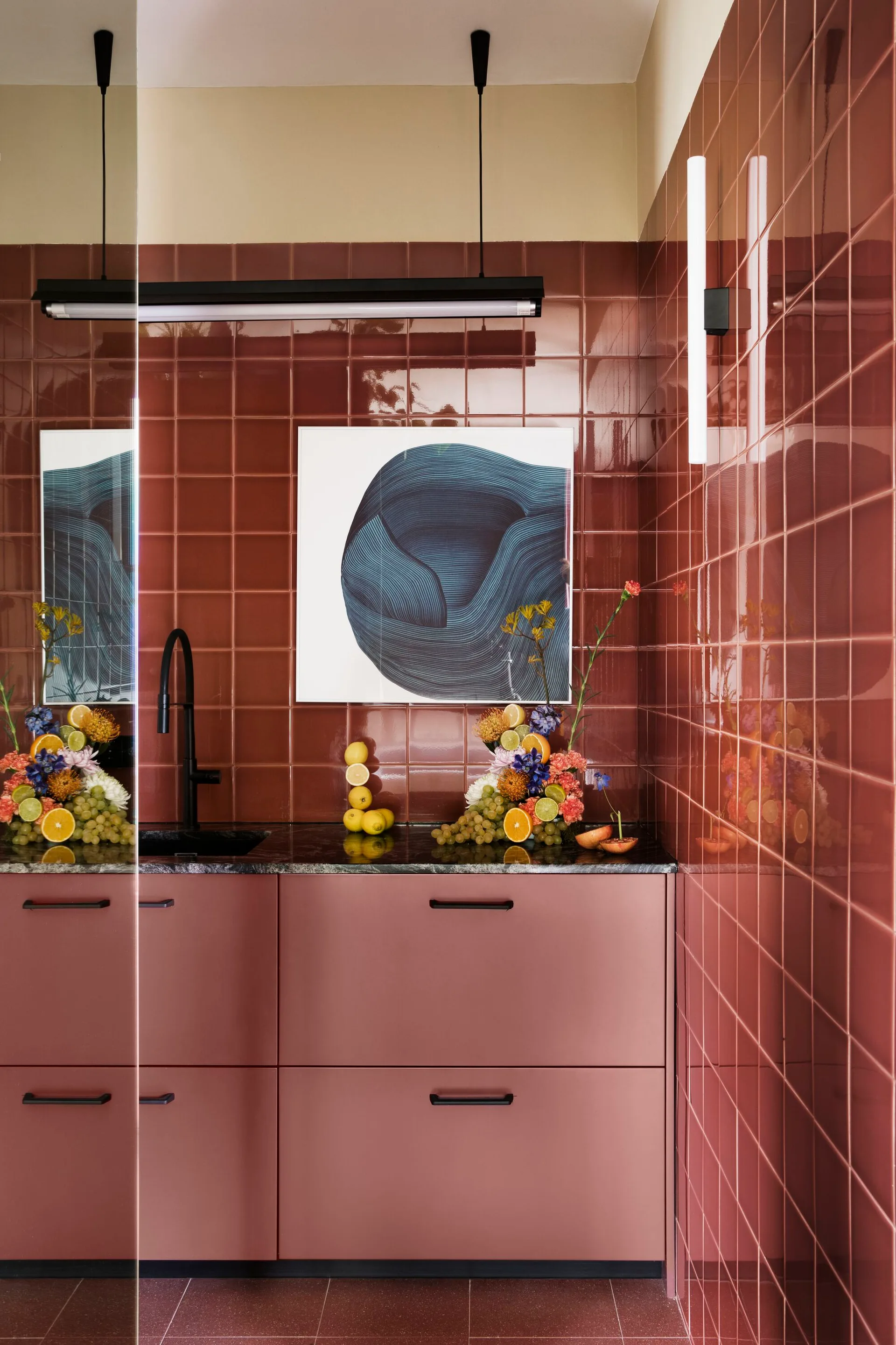 A modern kitchenette features matte terracotta cabinets, a dark stone countertop, a black faucet, and glossy square wall tiles.