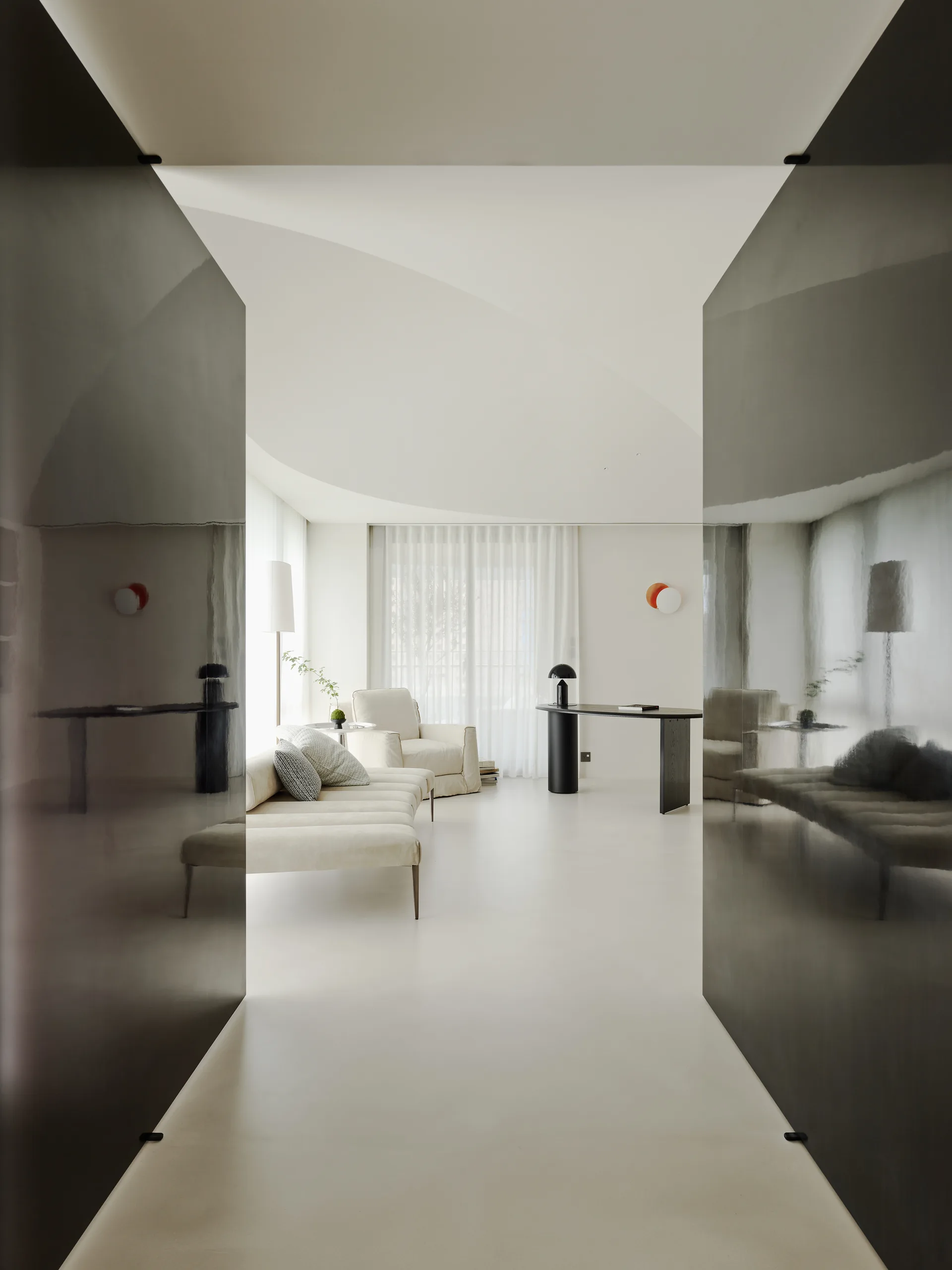 A view through a dark, reflective doorway into a bright minimalist living room with a curved ceiling, cream sofa, and sheer curtains.