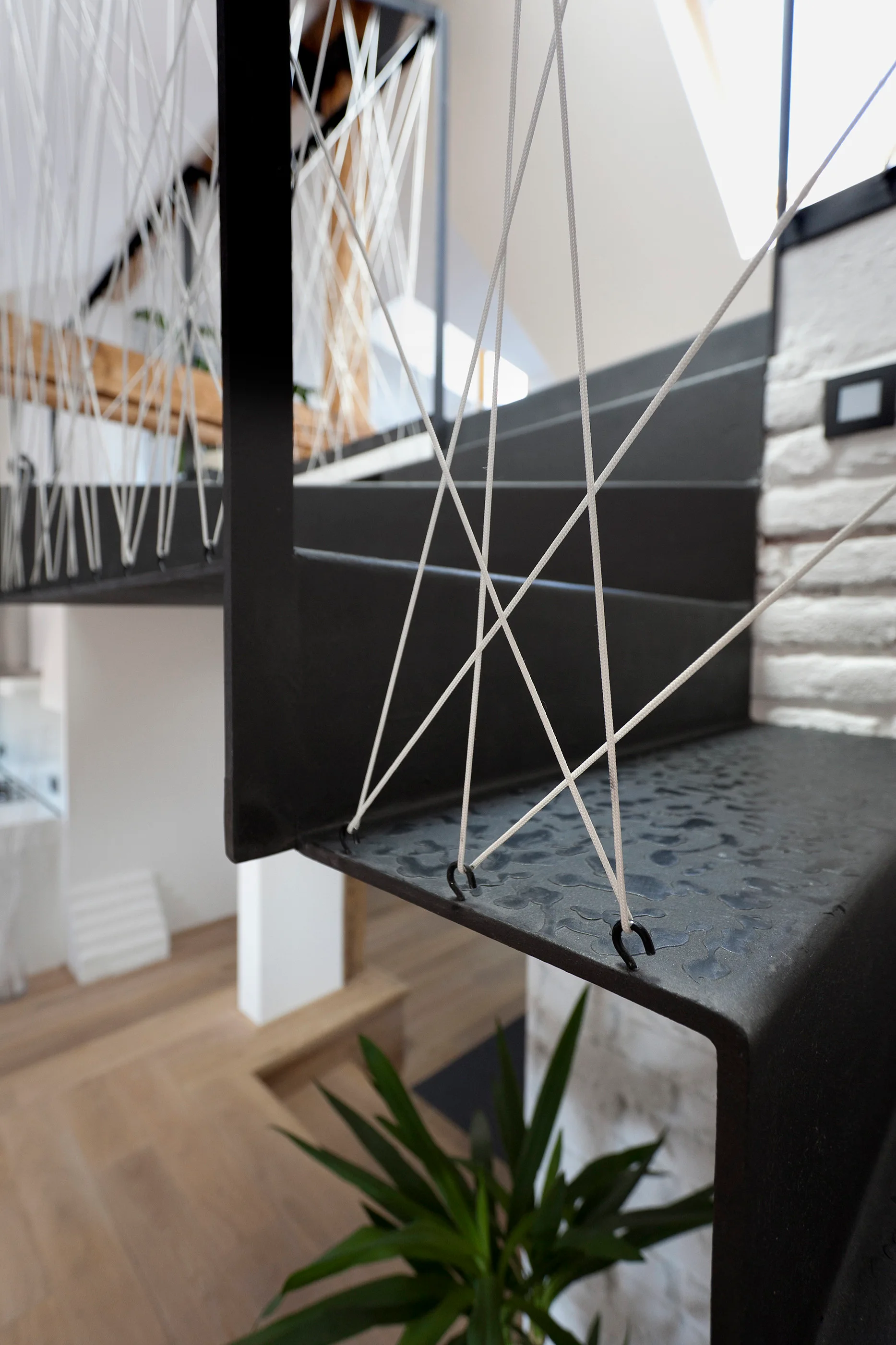 A close-up of a modern black metal staircase featuring a unique railing made of white tension cords threaded through eyelets on the steps.