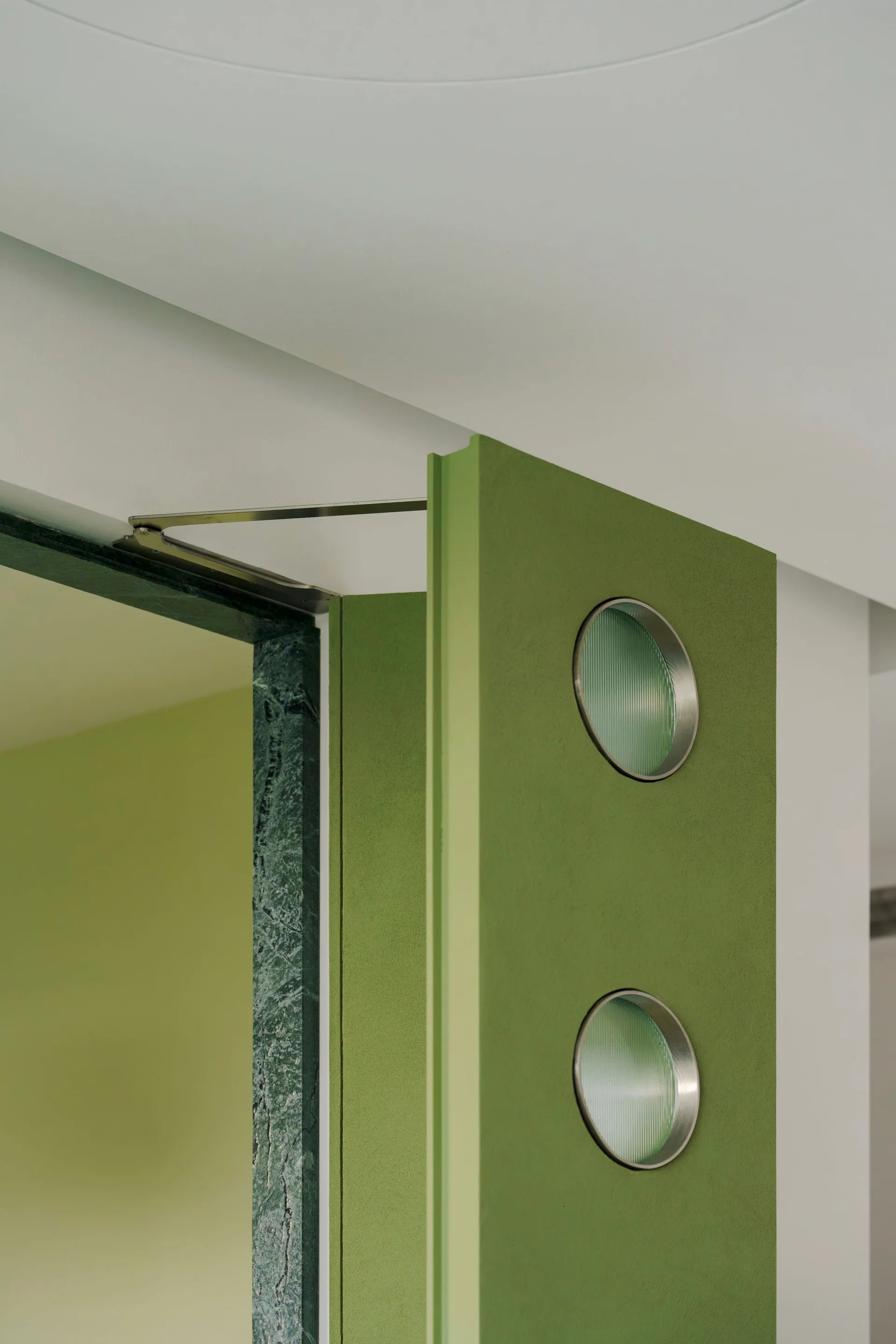 A matte olive green door featuring two circular ribbed glass porthole windows set against a dark green marble frame.