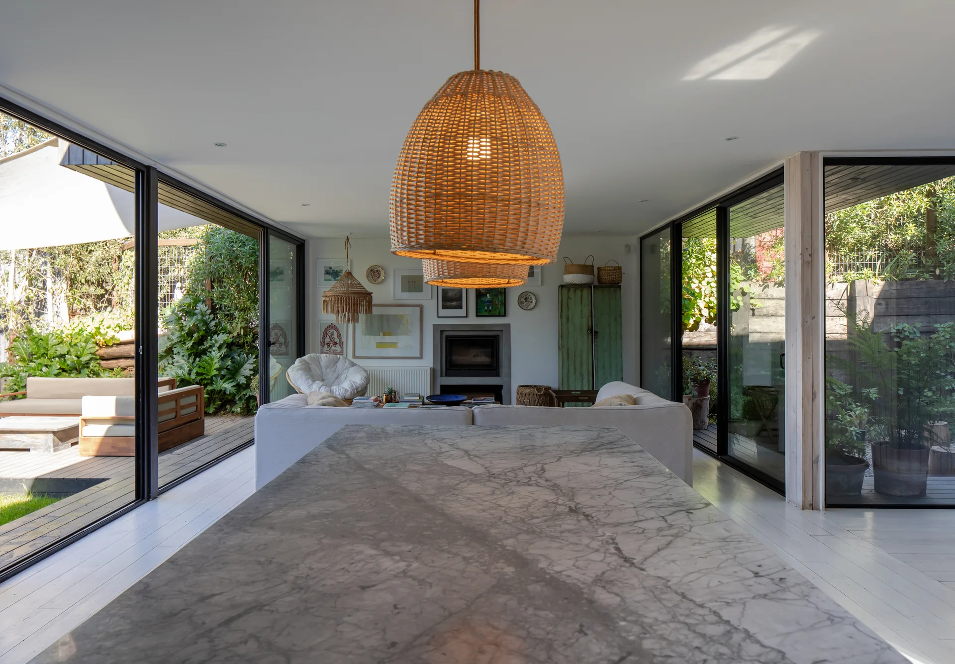 An open-concept living area features a marble island in the foreground, white sofa, and glass sliding doors that open to patio decks on both sides.