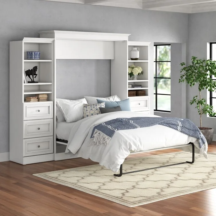 A bedroom features a white wood Murphy bed flanked by built-in bookcases with shelves and drawers on a hardwood floor over a geometric rug.