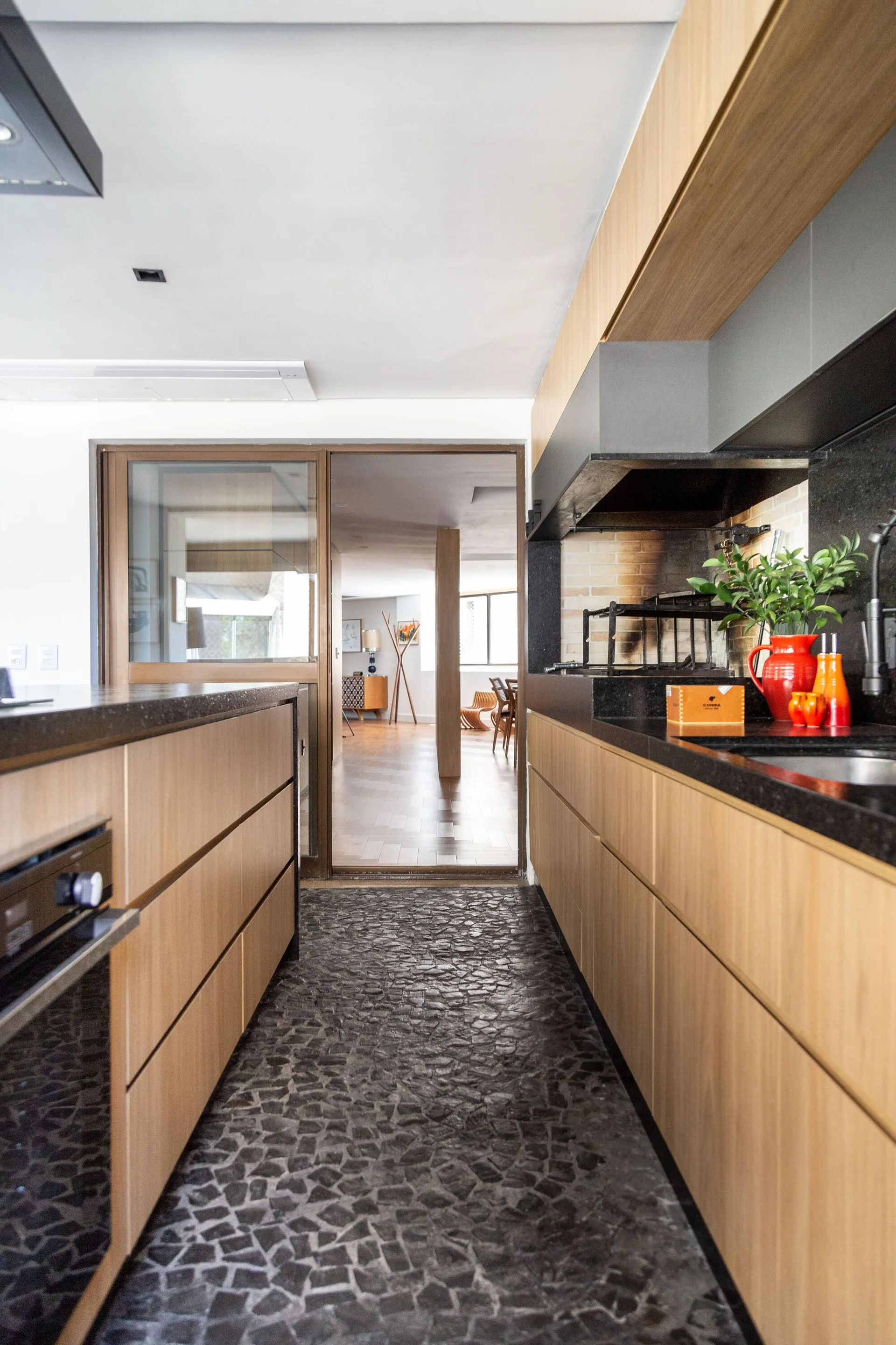 A galley kitchen features flat-front wood cabinetry, dark stone countertops, a textured cobblestone floor, and a sliding glass door.
