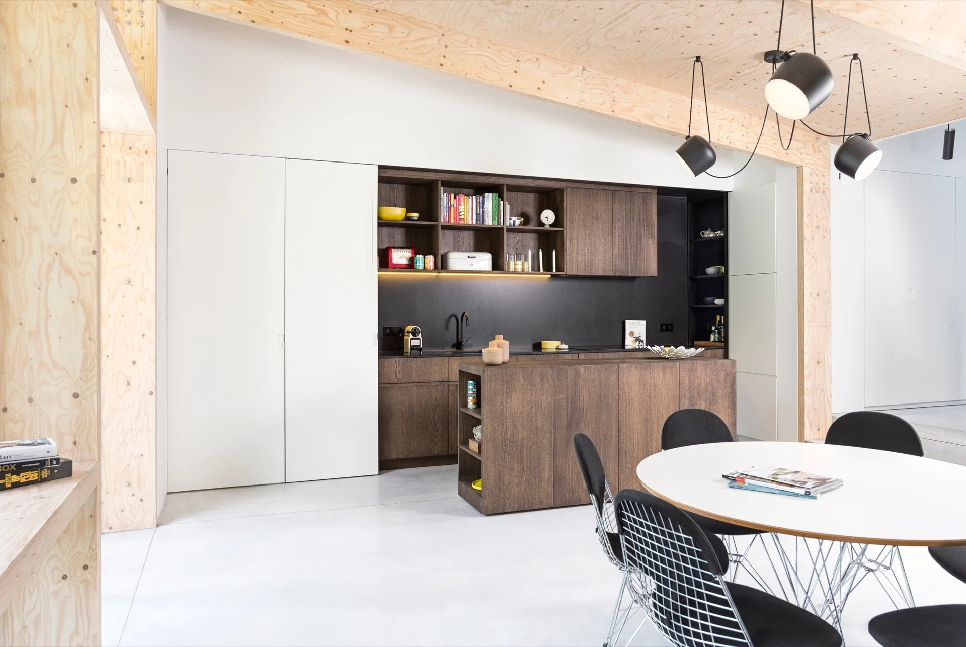A modern kitchen features dark wood cabinets, a matching island, a white round dining table, and a light-grained plywood ceiling.