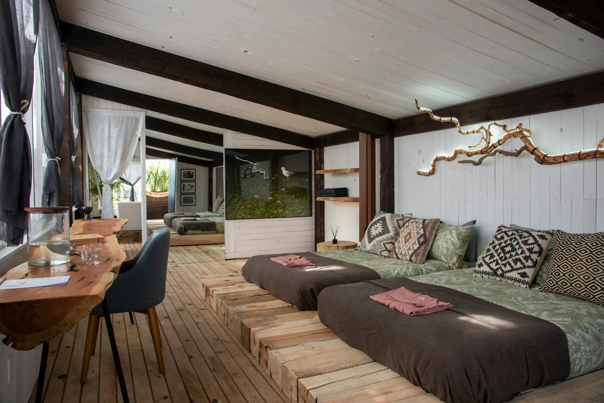 Two beds rest on a raw timber platform next to a live-edge wooden desk in a rustic cabin bedroom.