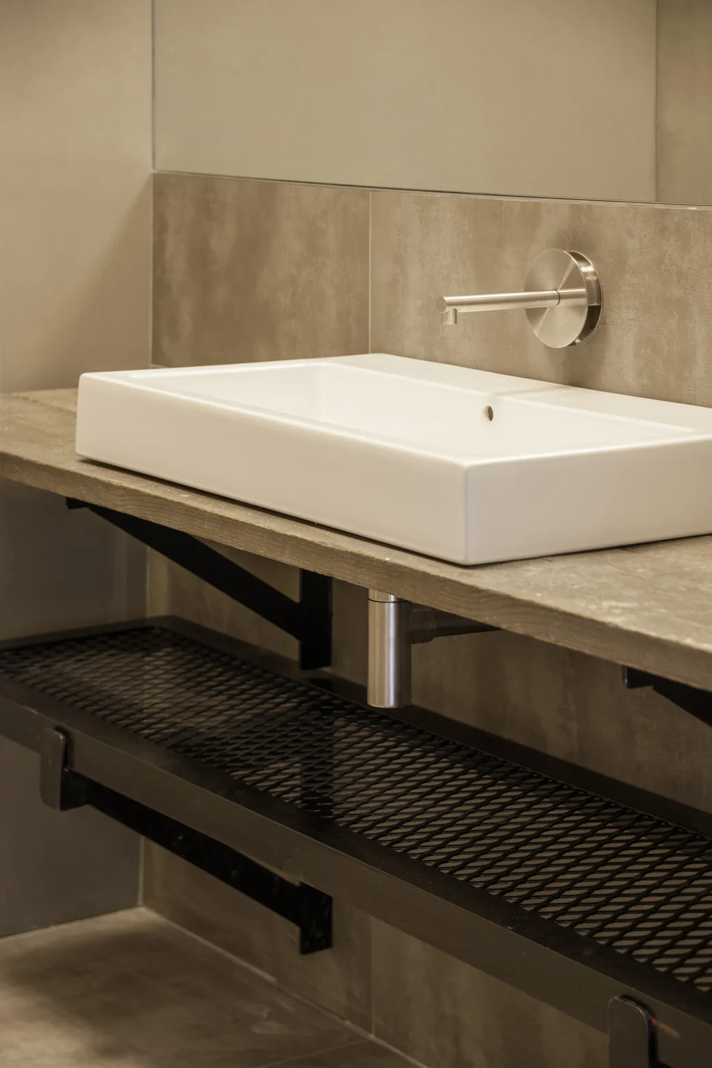 A white rectangular vessel sink sits on a concrete vanity countertop above a black metal mesh shelf.