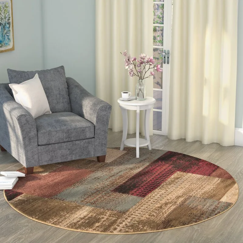 A grey upholstered armchair sits on a round patterned rug next to a white side table with flowers in a sunlit corner.
