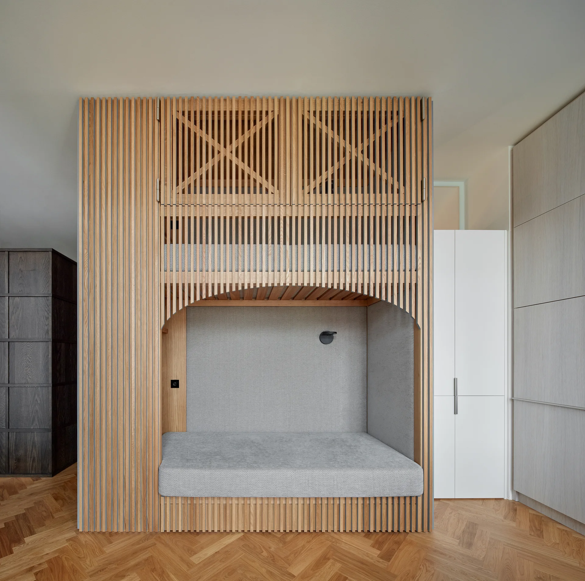 A custom light wood bunk bed structure with vertical slats and an arched opening on herringbone flooring.