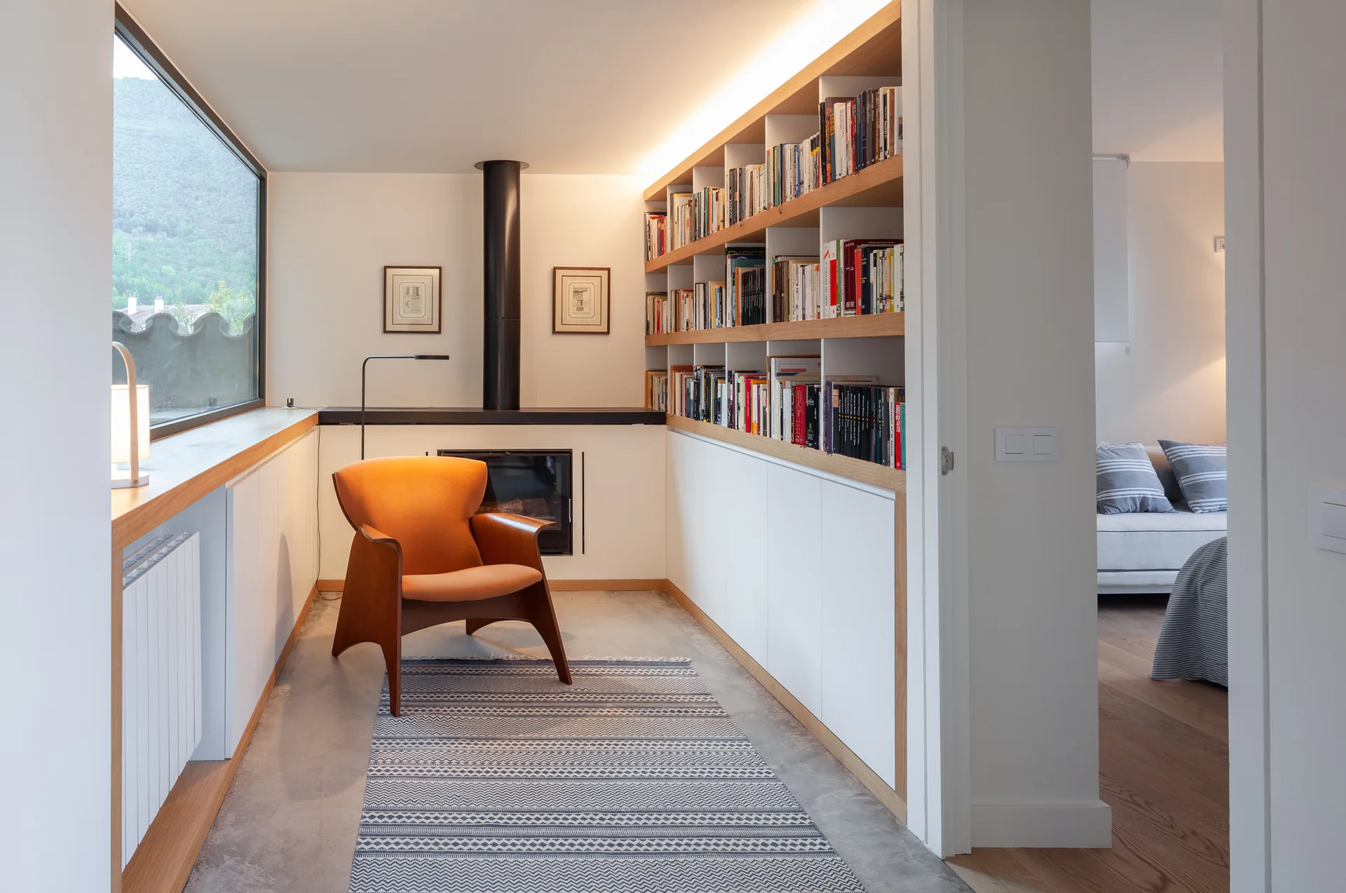 A reading nook featuring an orange mid-century modern lounge chair on a patterned rug next to built-in bookshelves and a fireplace.