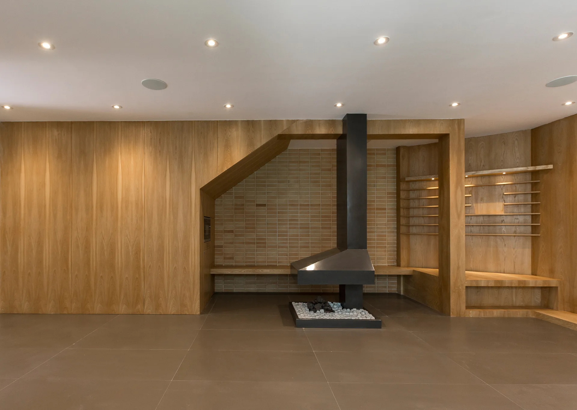 A minimalist room features a modern black metal fireplace set against a beige brick wall recessed inside a light wood paneled structure.