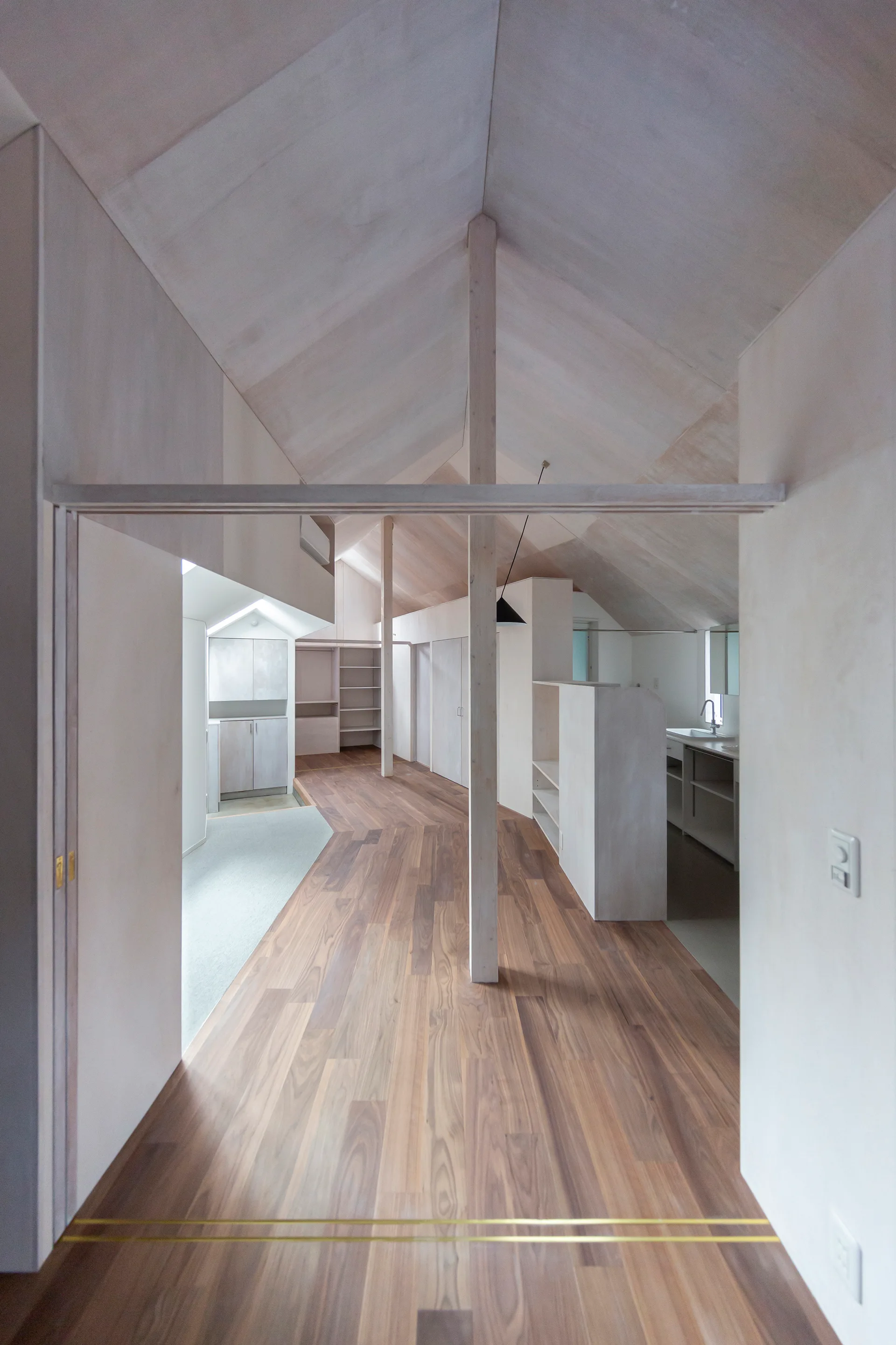 An open-concept minimalist loft space features a vaulted wood ceiling, exposed timber posts, and dark walnut flooring.