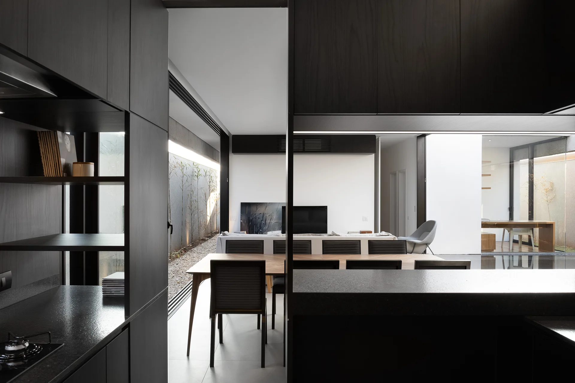 An open-concept kitchen features dark charcoal cabinetry, a wood dining table with chairs, and sliding glass doors opening to a gravel courtyard.