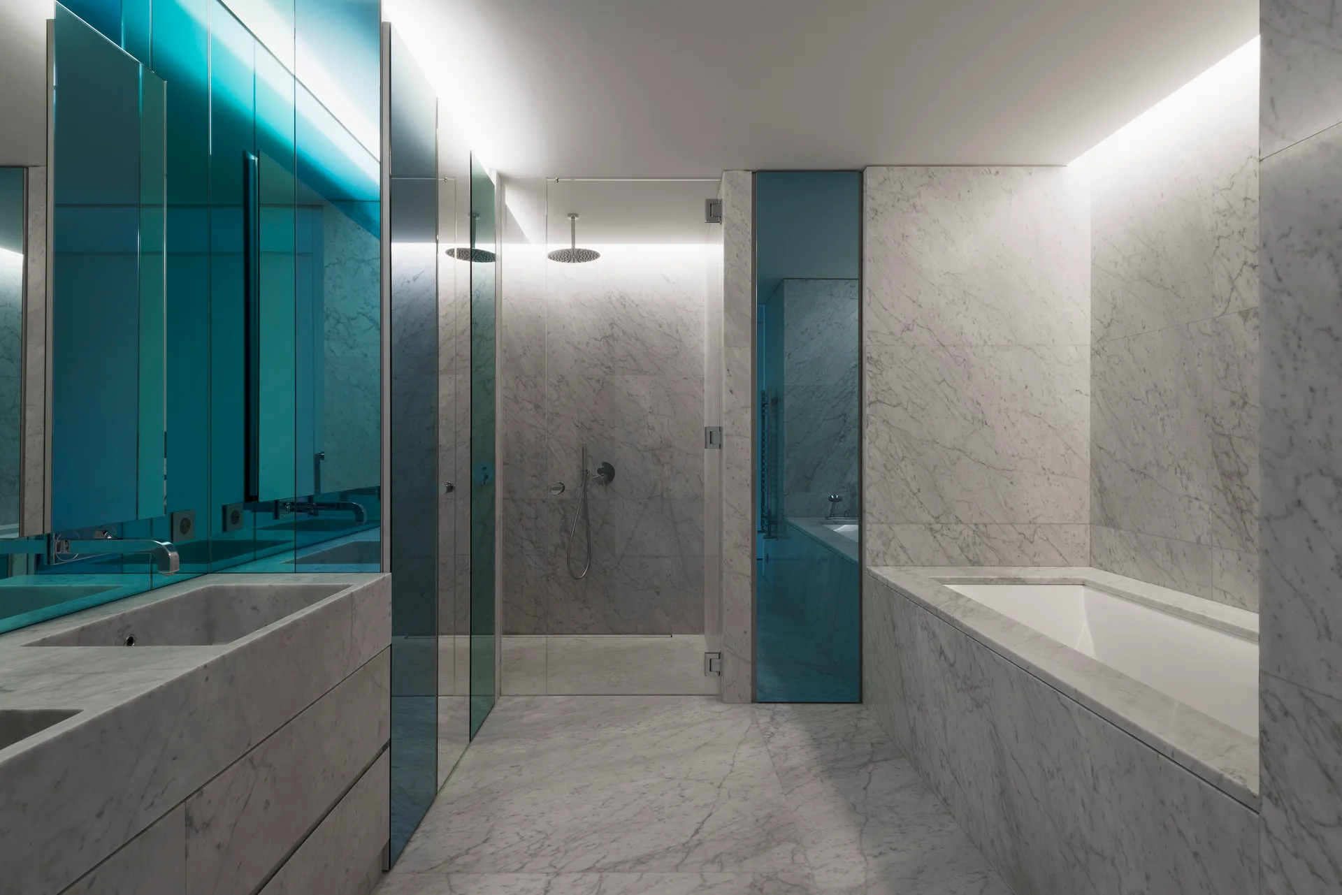 A modern bathroom lined in grey marble featuring a built-in tub, a glass-walled shower, and tall blue-tinted mirror panels.