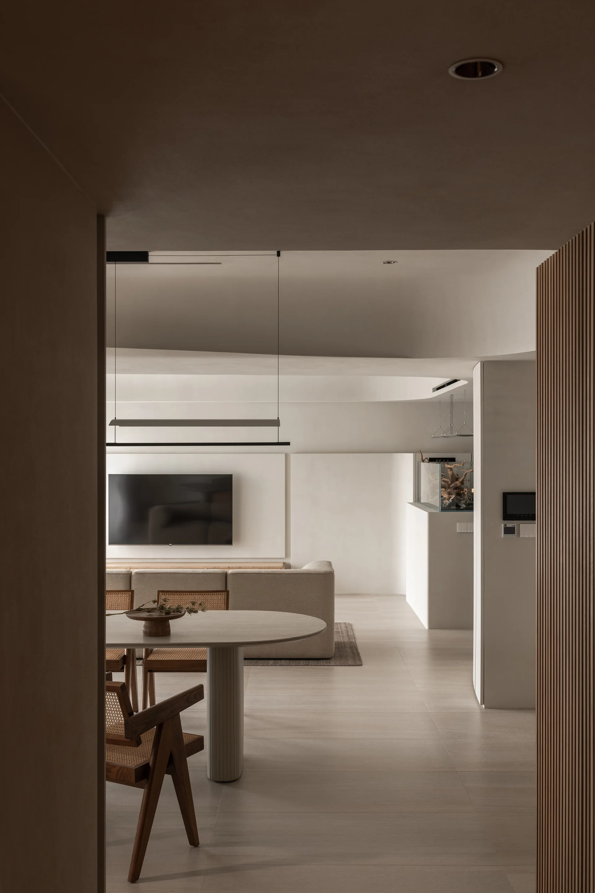 A minimalist open-plan living and dining area features a curved ceiling, a round dining table with cane chairs, and a beige sofa.