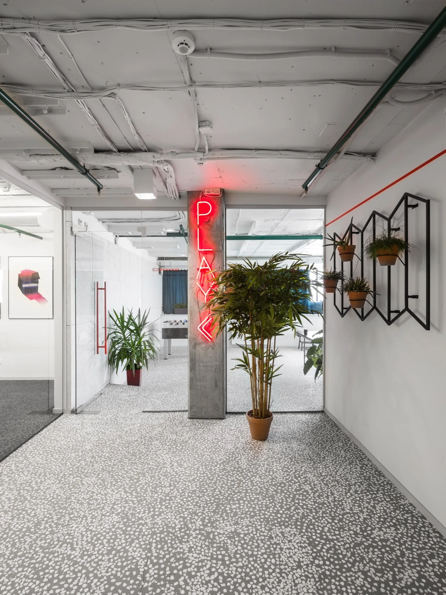 A modern commercial entryway with speckled terrazzo flooring, an exposed concrete pillar with a red neon sign, and a geometric wall planter.