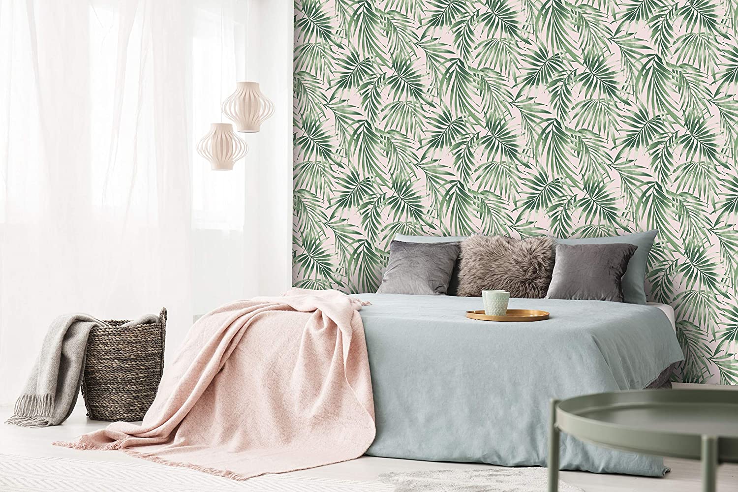 A modern bedroom features green palm leaf patterned wallpaper behind a bed dressed in light blue linens, grey decorative pillows, and a pink throw blanket.