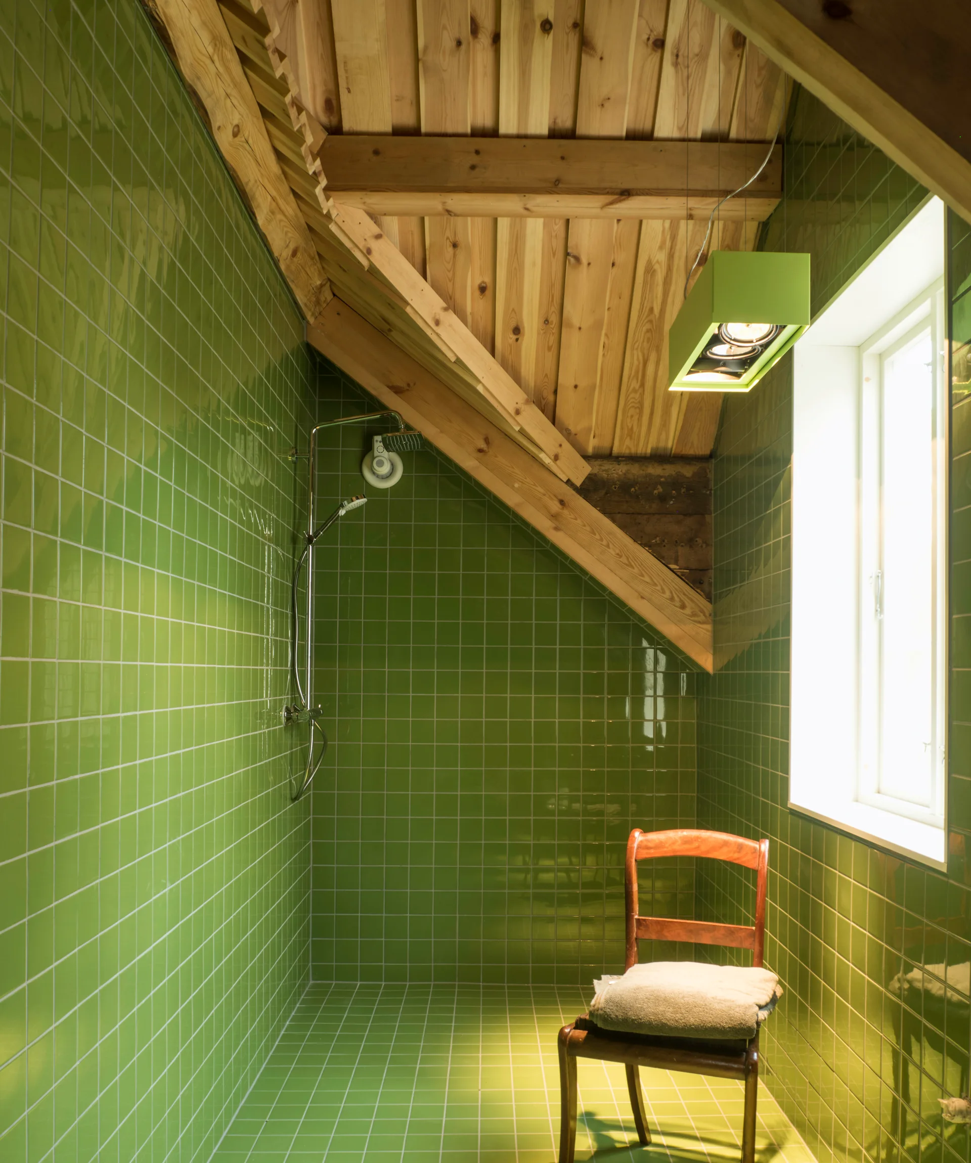 A bathroom featuring glossy green square tiles on the walls and floor beneath a vaulted raw wood plank ceiling with exposed timber beams.