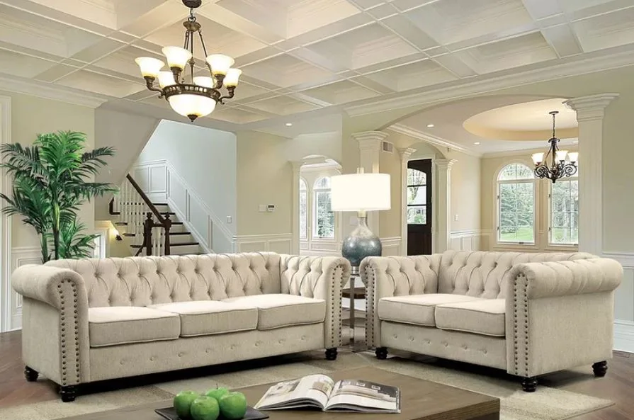 A formal living room featuring two tufted beige sofas, a white coffered ceiling, and a wooden coffee table.
