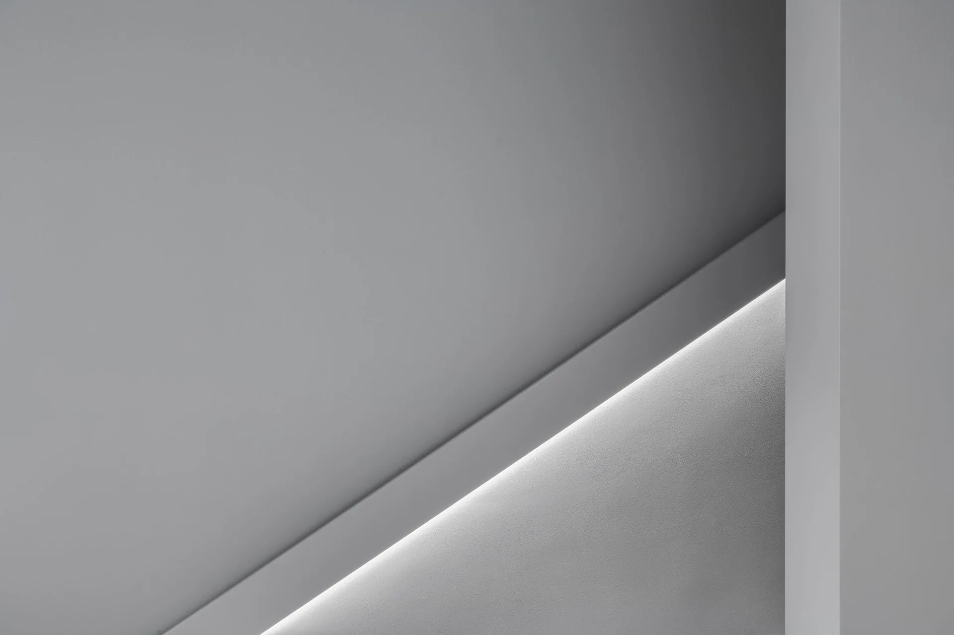 Close-up of a minimalist gray wall featuring a diagonal recessed channel with integrated linear cove lighting.