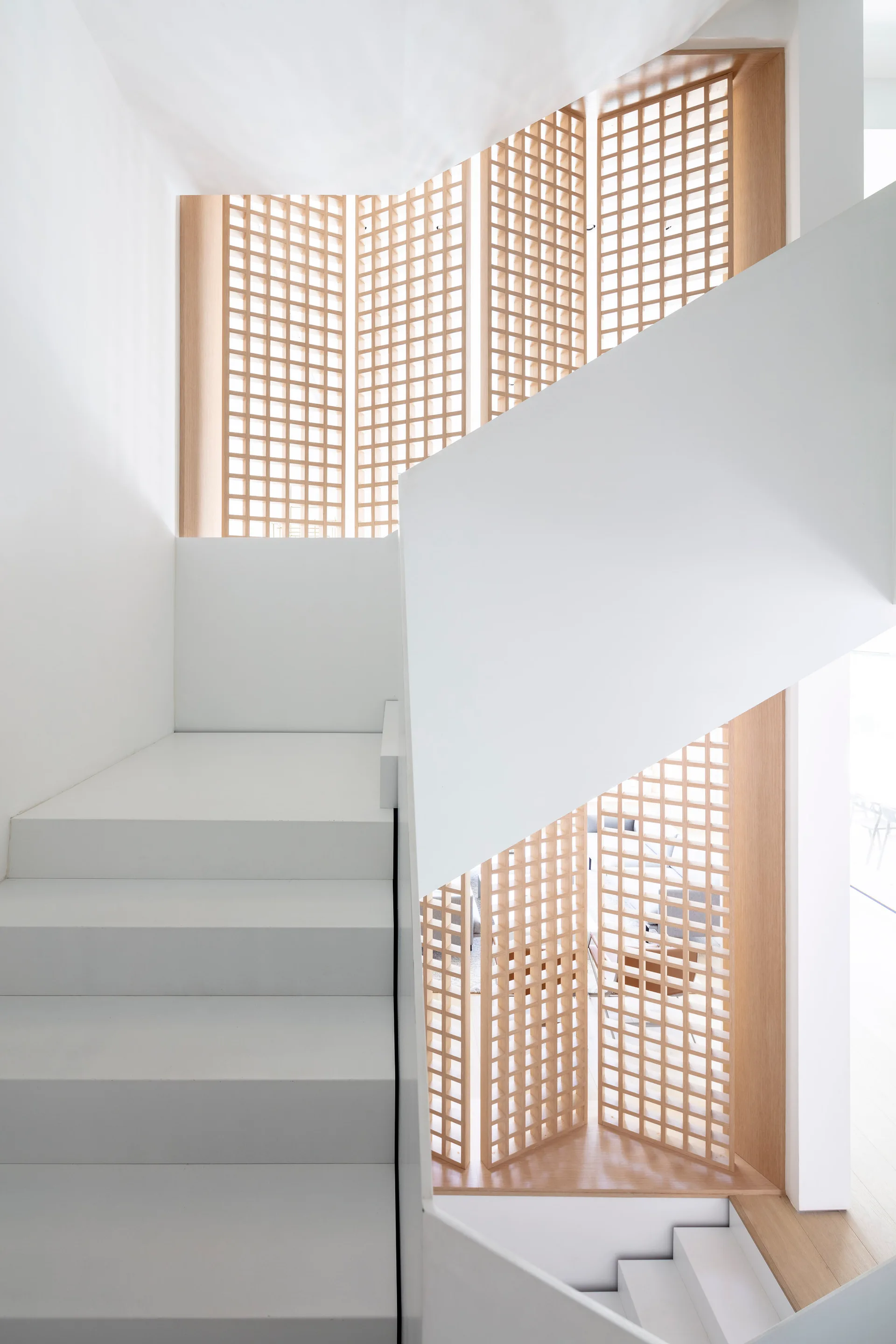 A modern white staircase winds past warm wood geometric lattice screens in a minimalist home stairwell.