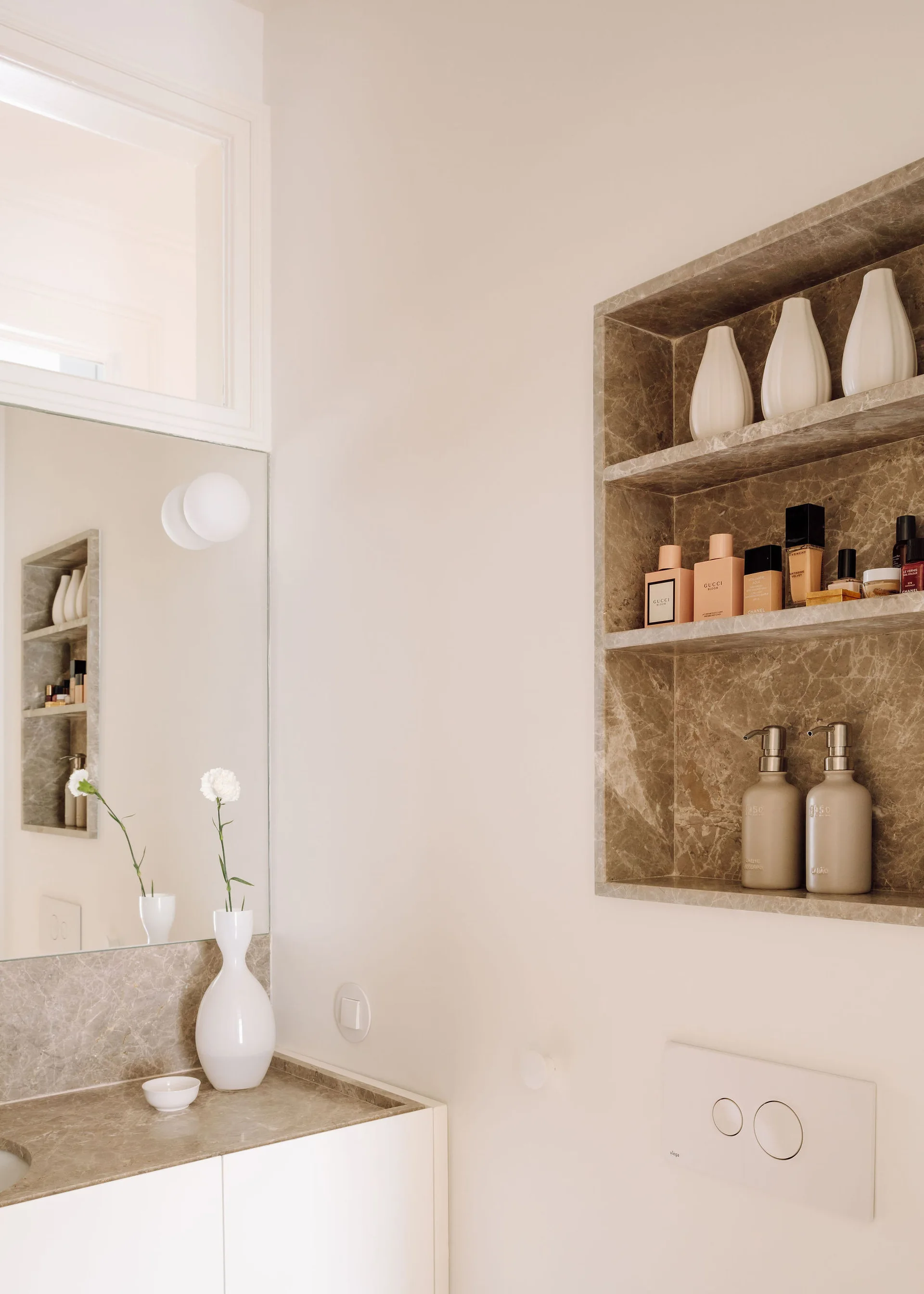A modern bathroom vanity with a taupe stone countertop and a matching recessed stone wall niche holding toiletries and white vases.