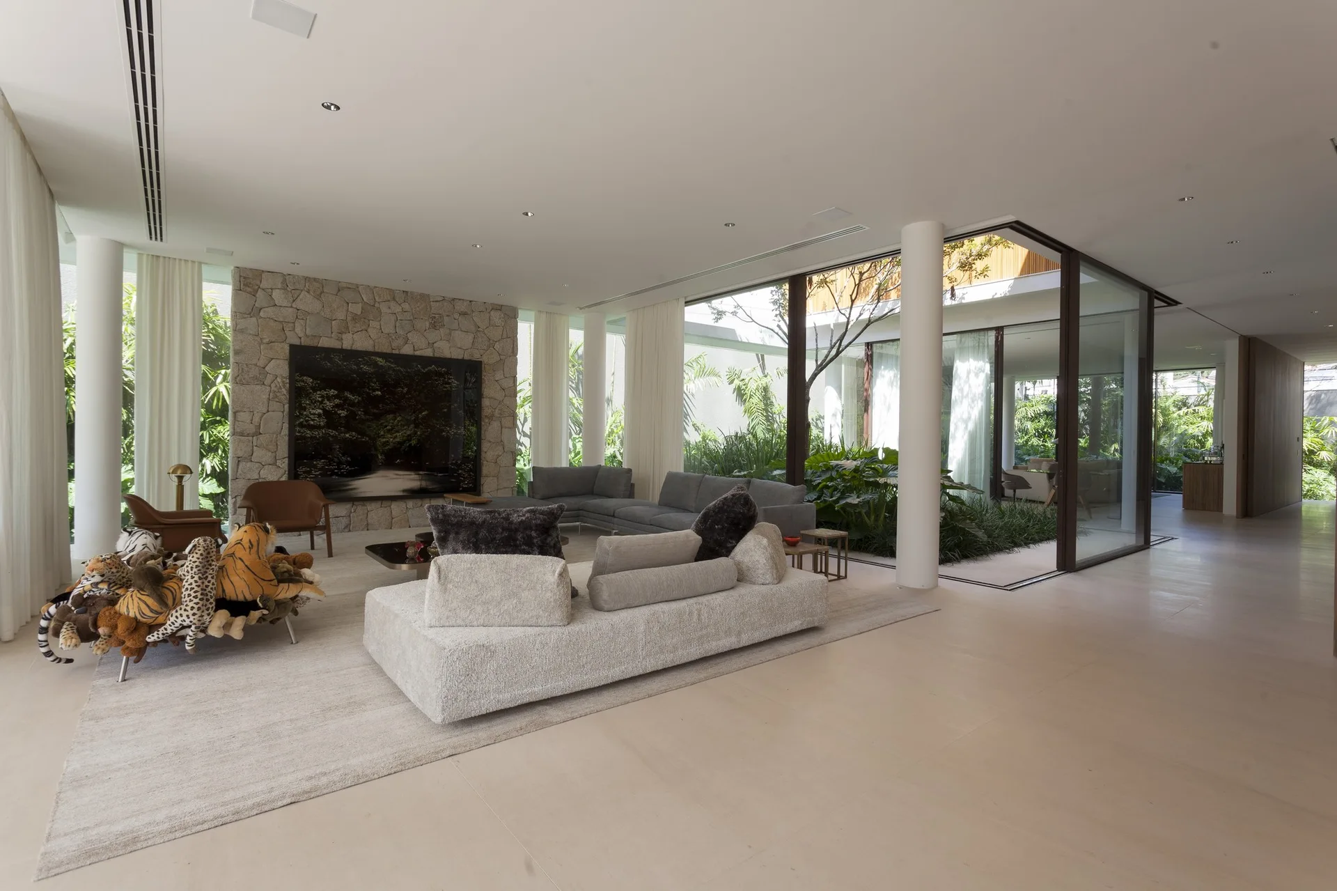 A spacious modern living room with low-profile sectional sofas, a natural stone feature wall, and floor-to-ceiling glass looking onto a lush indoor garden.