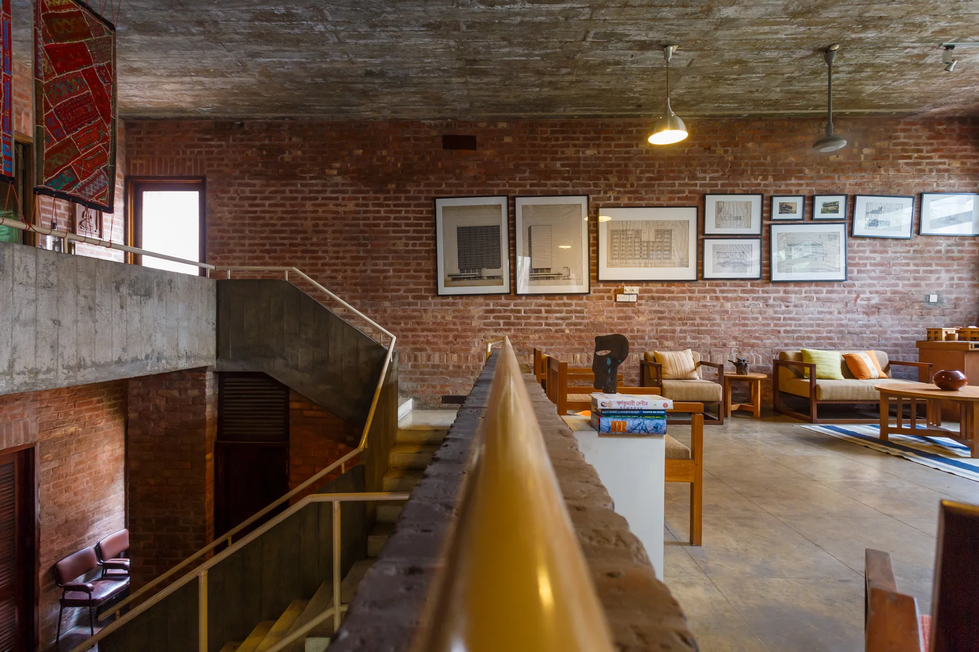 A split-level living area features exposed red brick walls, an unfinished concrete ceiling, wooden mid-century furniture, and a concrete staircase.