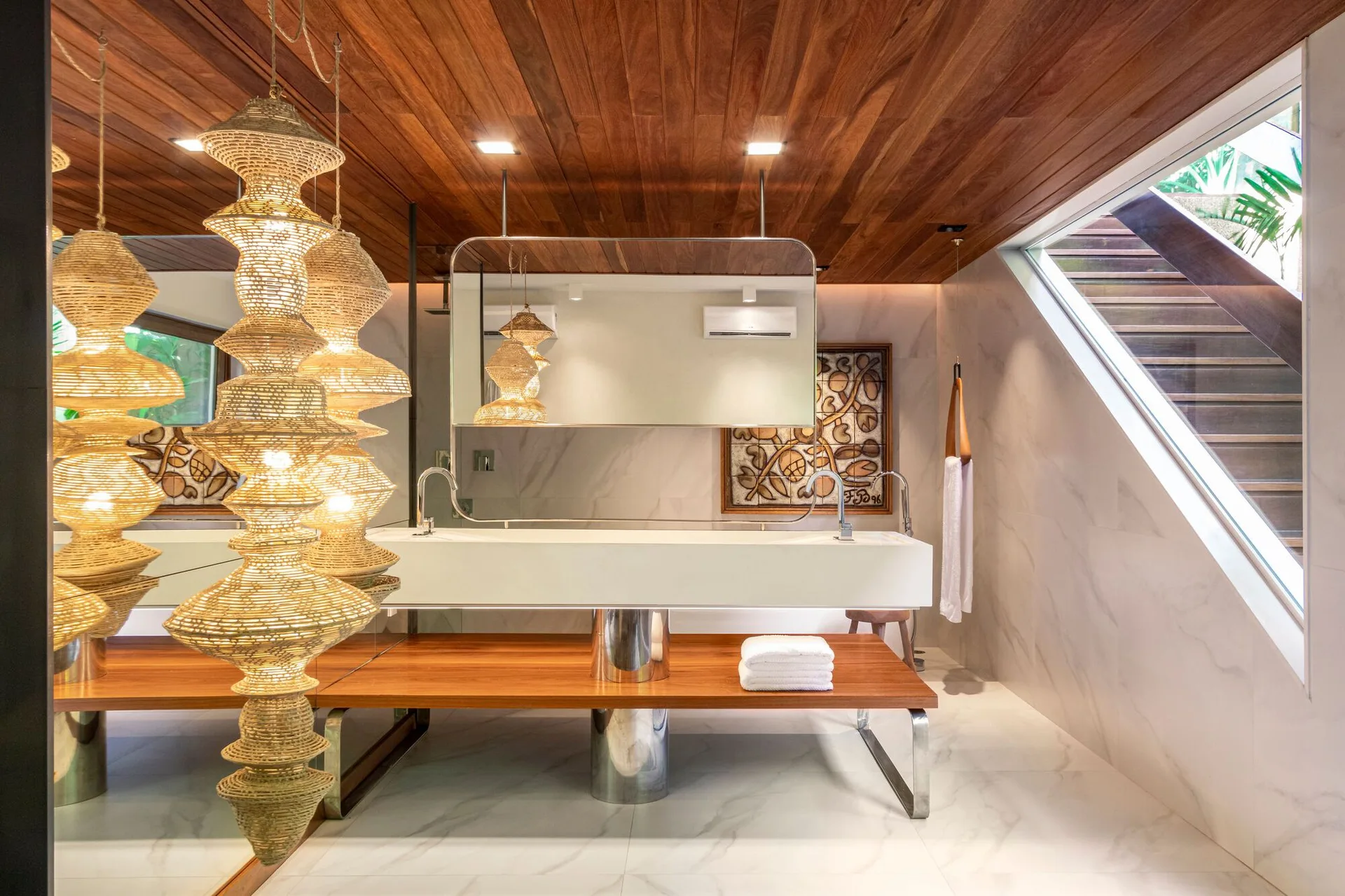 A modern bathroom featuring a white trough vanity, a warm wood plank ceiling, stone-look walls, and a large woven pendant light fixture.