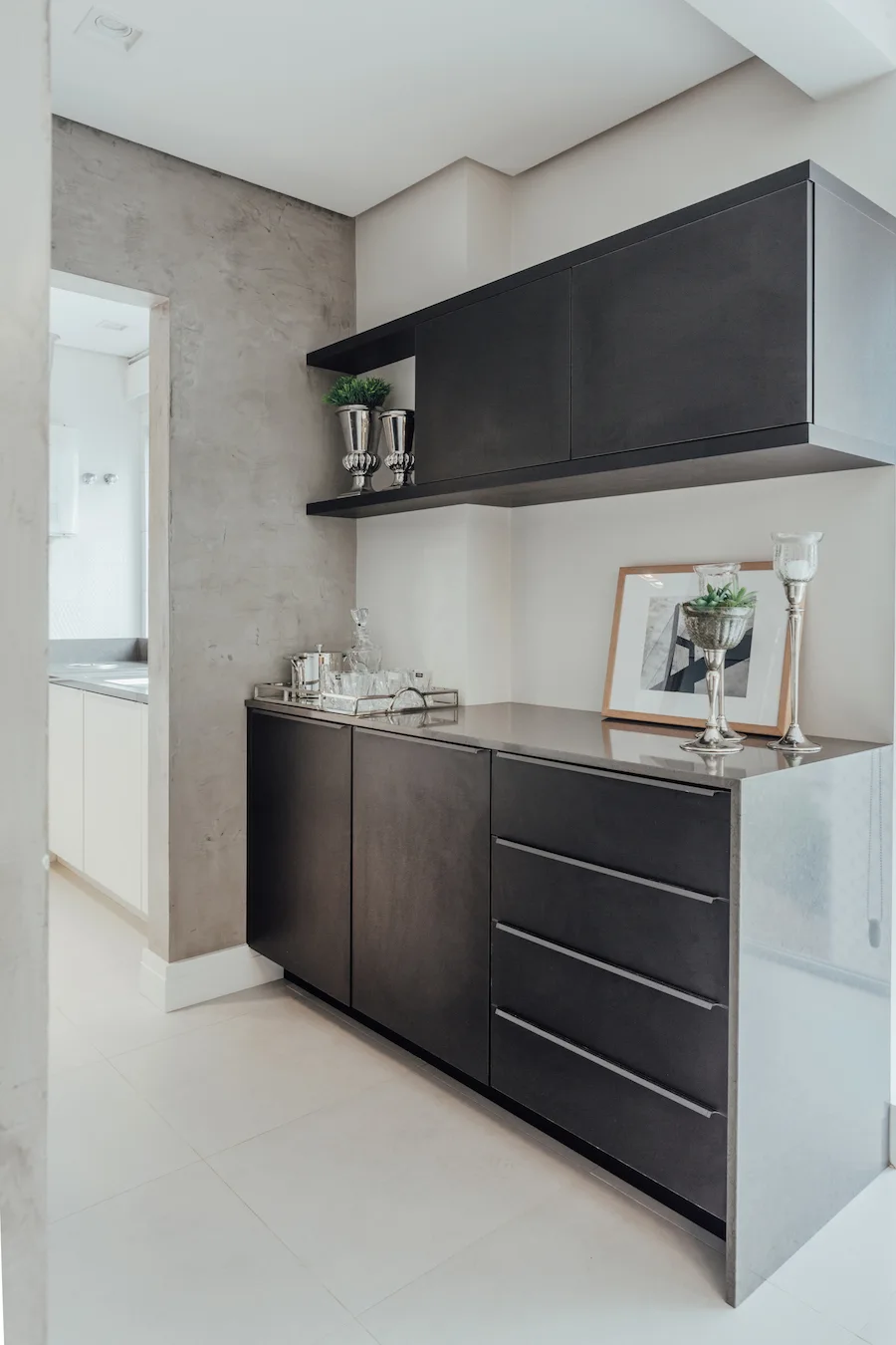 A modern home bar features matte black cabinetry, a gray concrete accent wall, a glossy countertop with glassware, and metallic decor accents.
