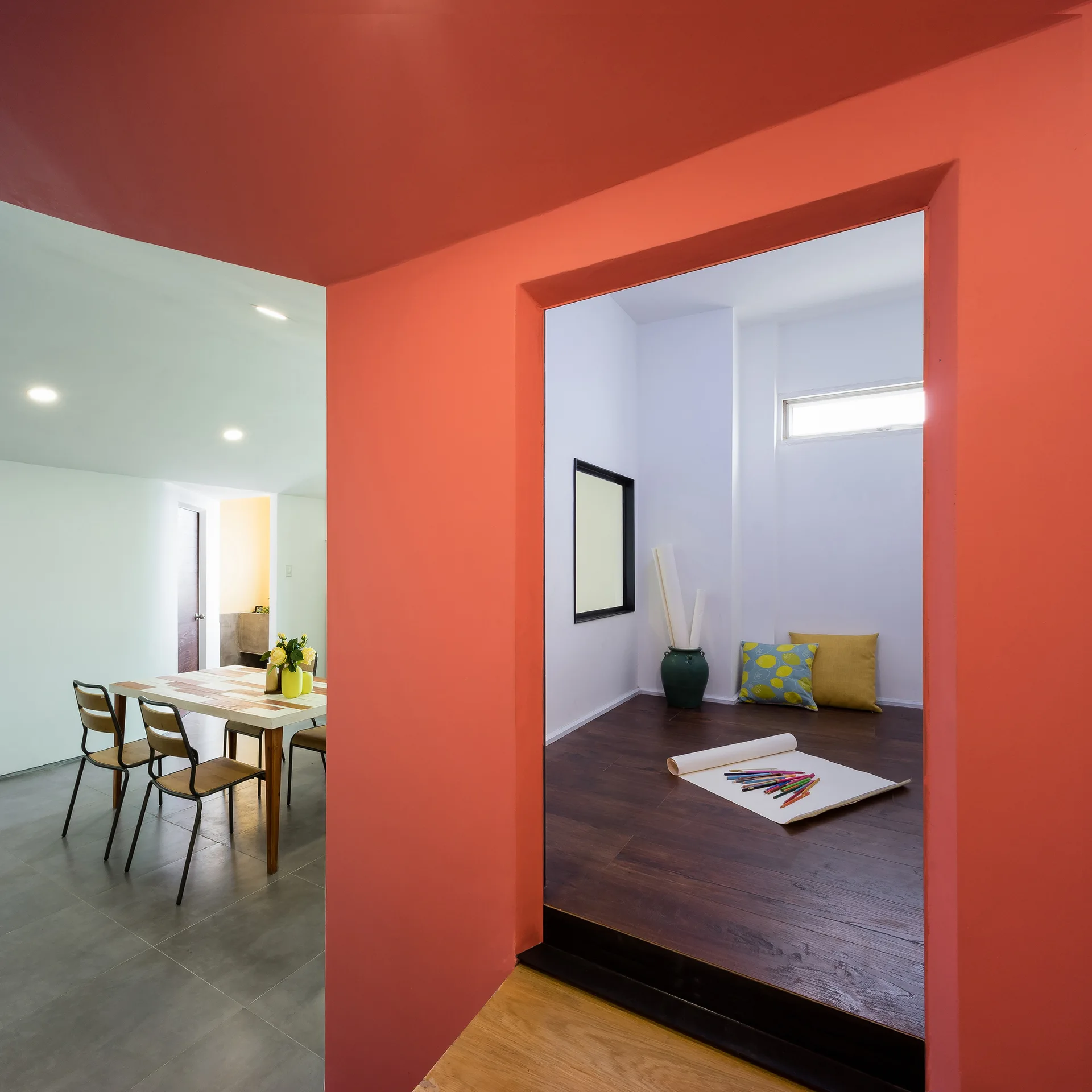 A view through a bold coral doorway showing a raised alcove with dark wood floors on the right and a dining area with gray tiles on the left.