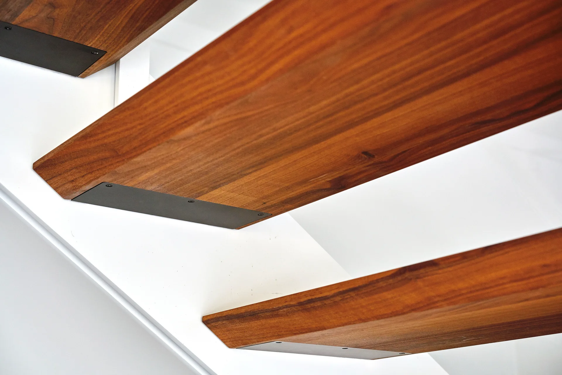 Close-up of wooden floating stair treads with black metal brackets flush mounted underneath against a white wall.