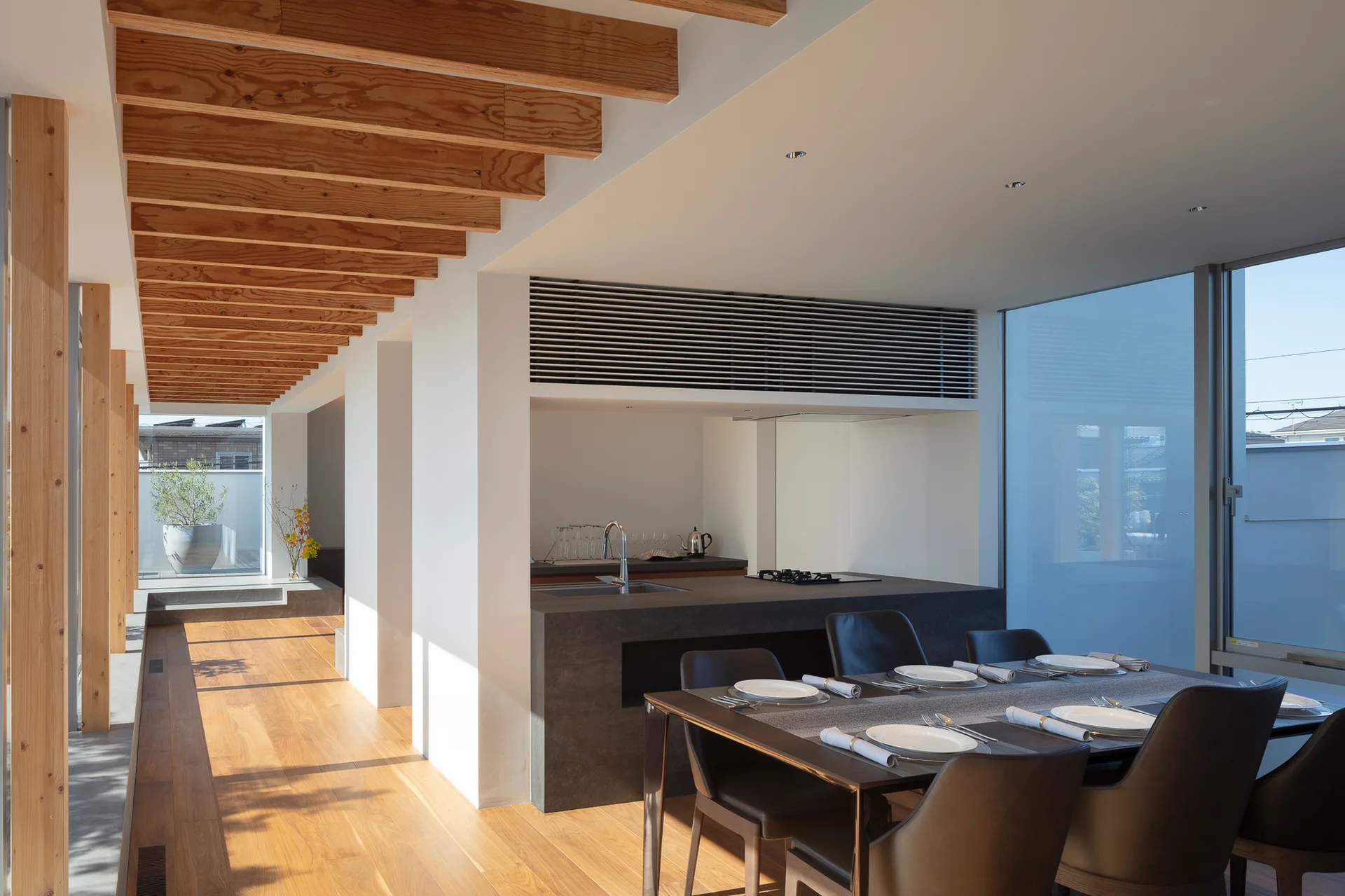 A modern kitchen and dining space with exposed wood ceiling beams, a dark charcoal island, and a dining table set for dinner.
