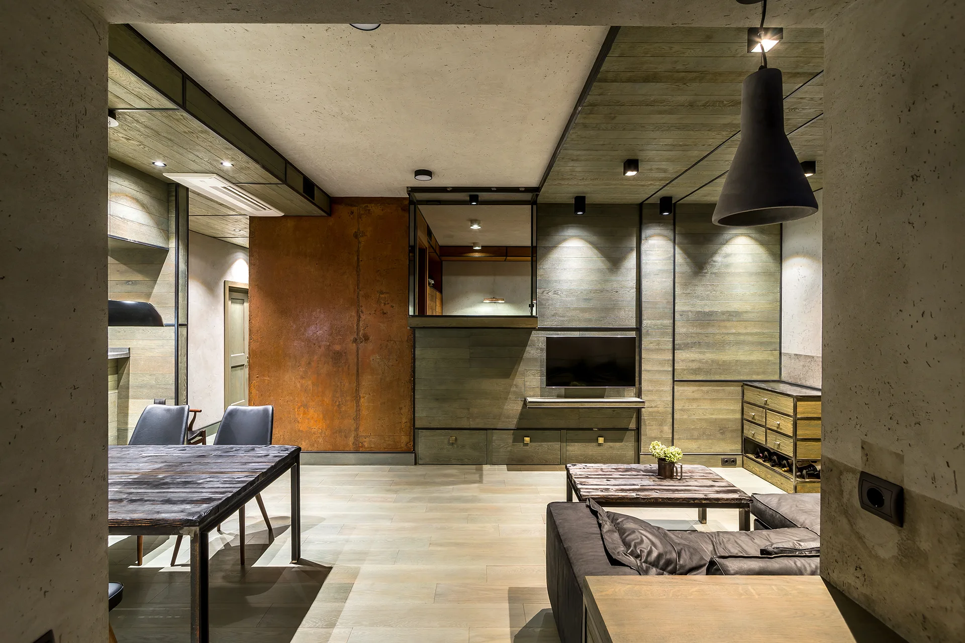 An industrial open-plan living room features a dark leather sofa, a rustic wooden dining table, a rusted metal wall panel, and weathered wood wall slats.